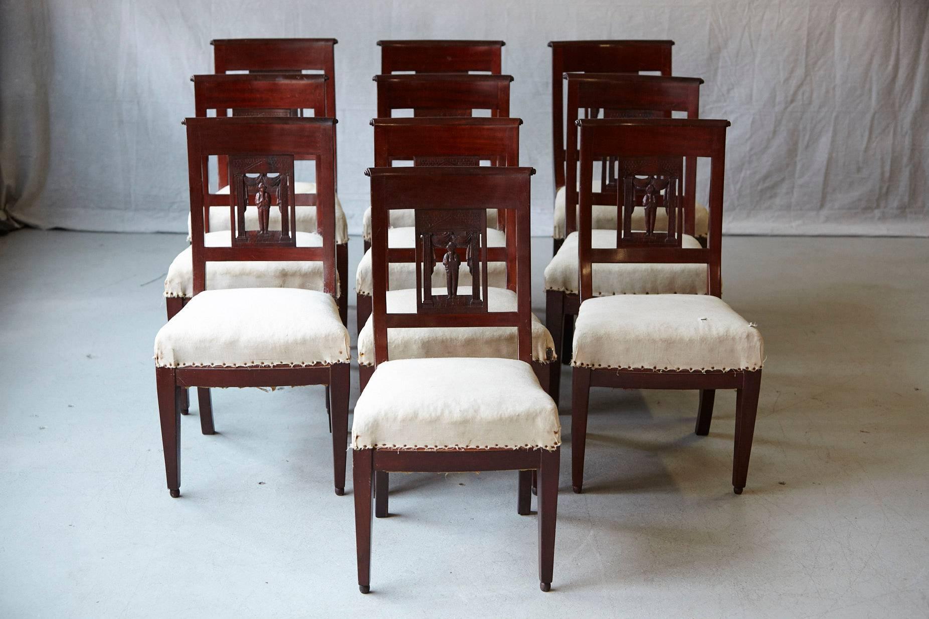 Beautiful set of ten antique mahogany dining chairs with a carved back depicting a figure beneath draped curtain, presently covered in sand colored muslin.
The chairs have a distressed appearance, the muslin on some of the chairs has stains, on has