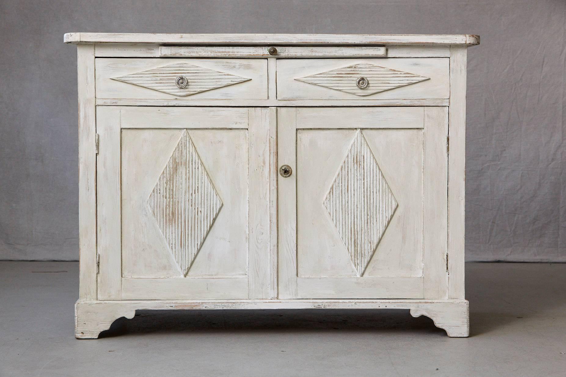 Swedish sideboard from the Gustavian period, two doors with diamond shaped and reeded carvings, which open into a single shelf. Two drawers also with diamond shaped and reeded carvings above with an additional integrated serving tray. All