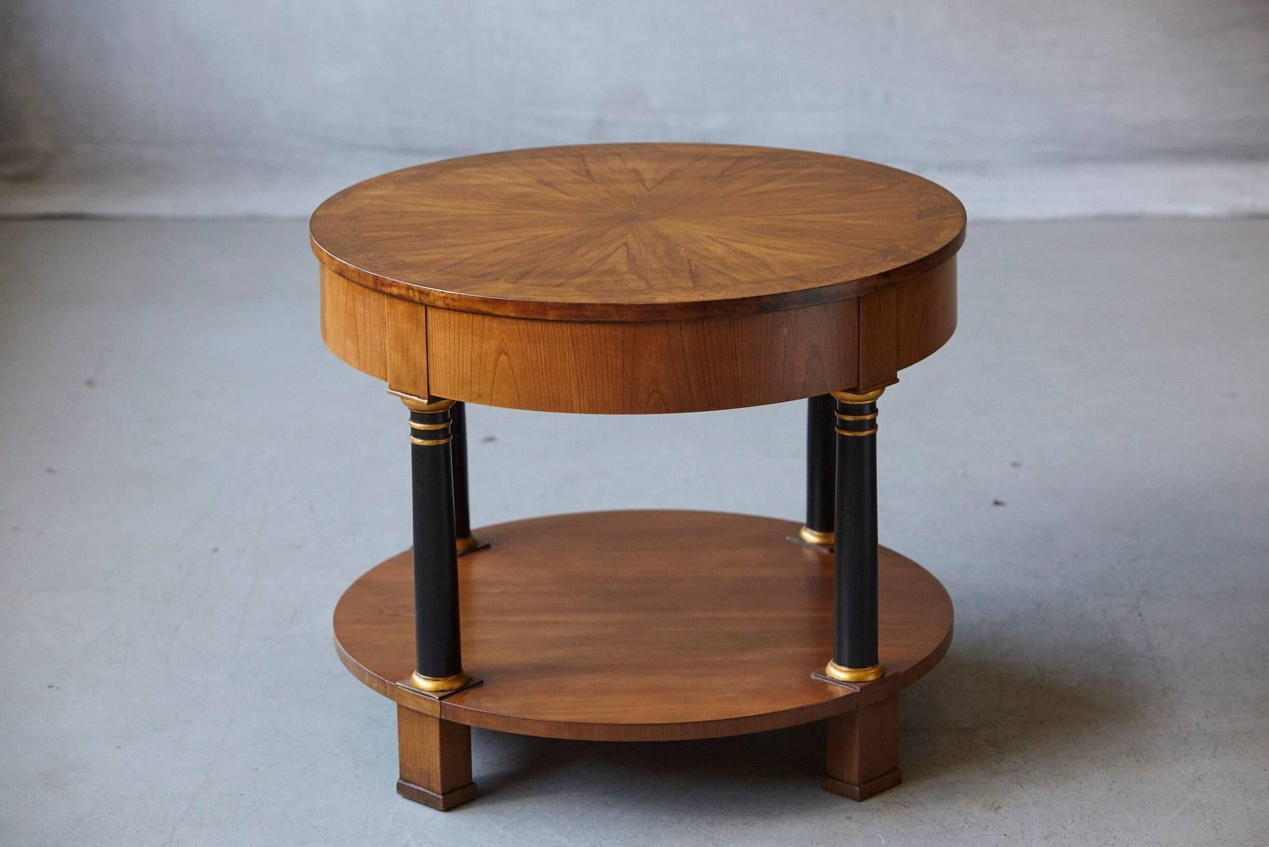 Very fine round Empire style two-tier walnut side or end table with one drawer by Baker Furniture, circa 1970s. Sunburst walnut veneer top, black lacquered columns with guilt accents. Drawer with original brass hardware. The Baker metal sign on the