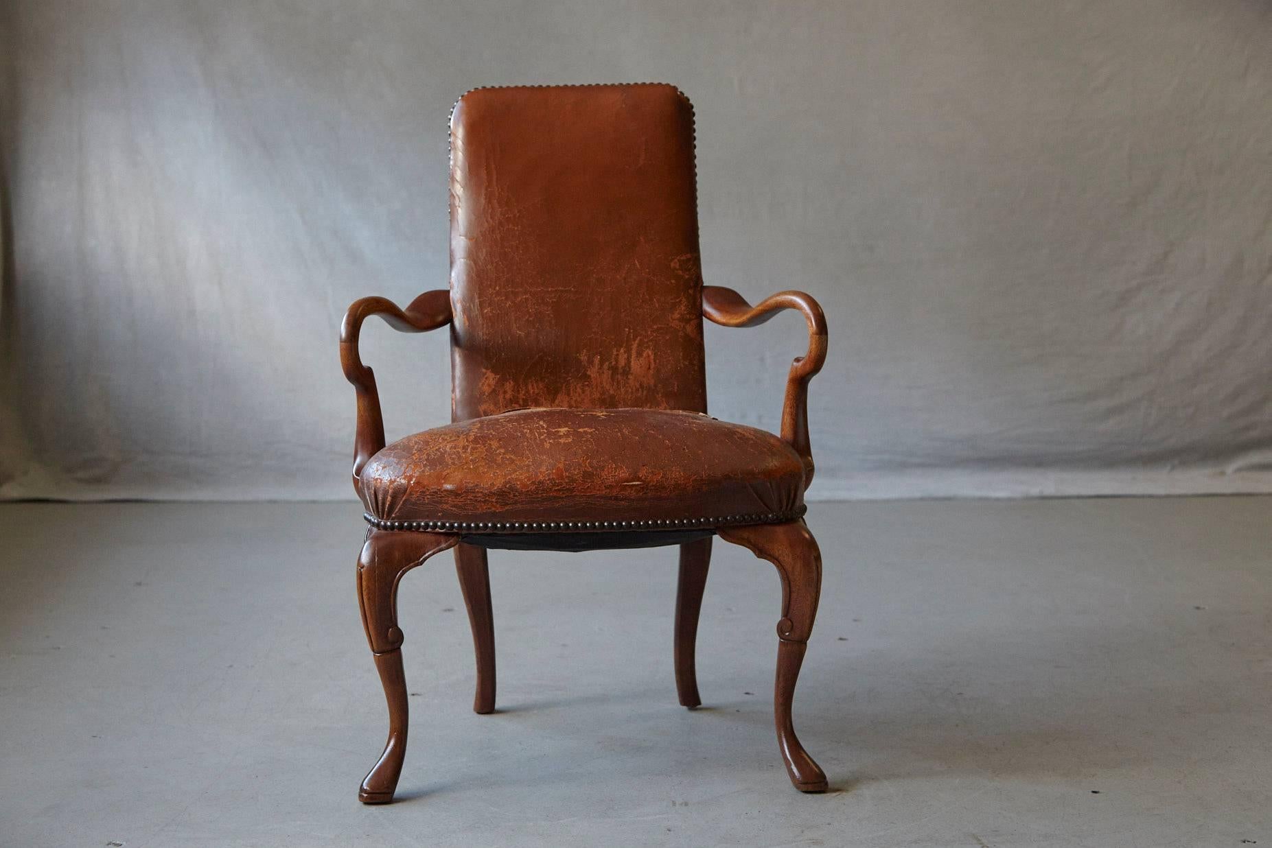 Lovely antique solid mahogany George III style desk armchair, with distressed worn hand dyed leather upholstery, nailhead trim and shaped arms. The chair is raised on cabriole legs with carved knees. 
The chair is in very good solid condition and