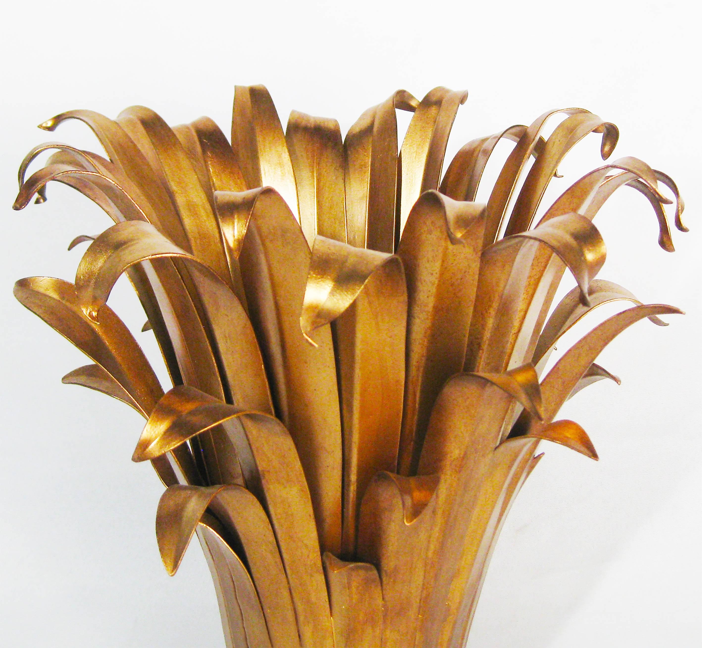 A gilded table lamp of delicately patinated metals that depicts pandanus leaves (or the like!) bound by ribbon. The subtle, textured effect of the light's reflection as it passes out through these layered golden blades is lovely and pure