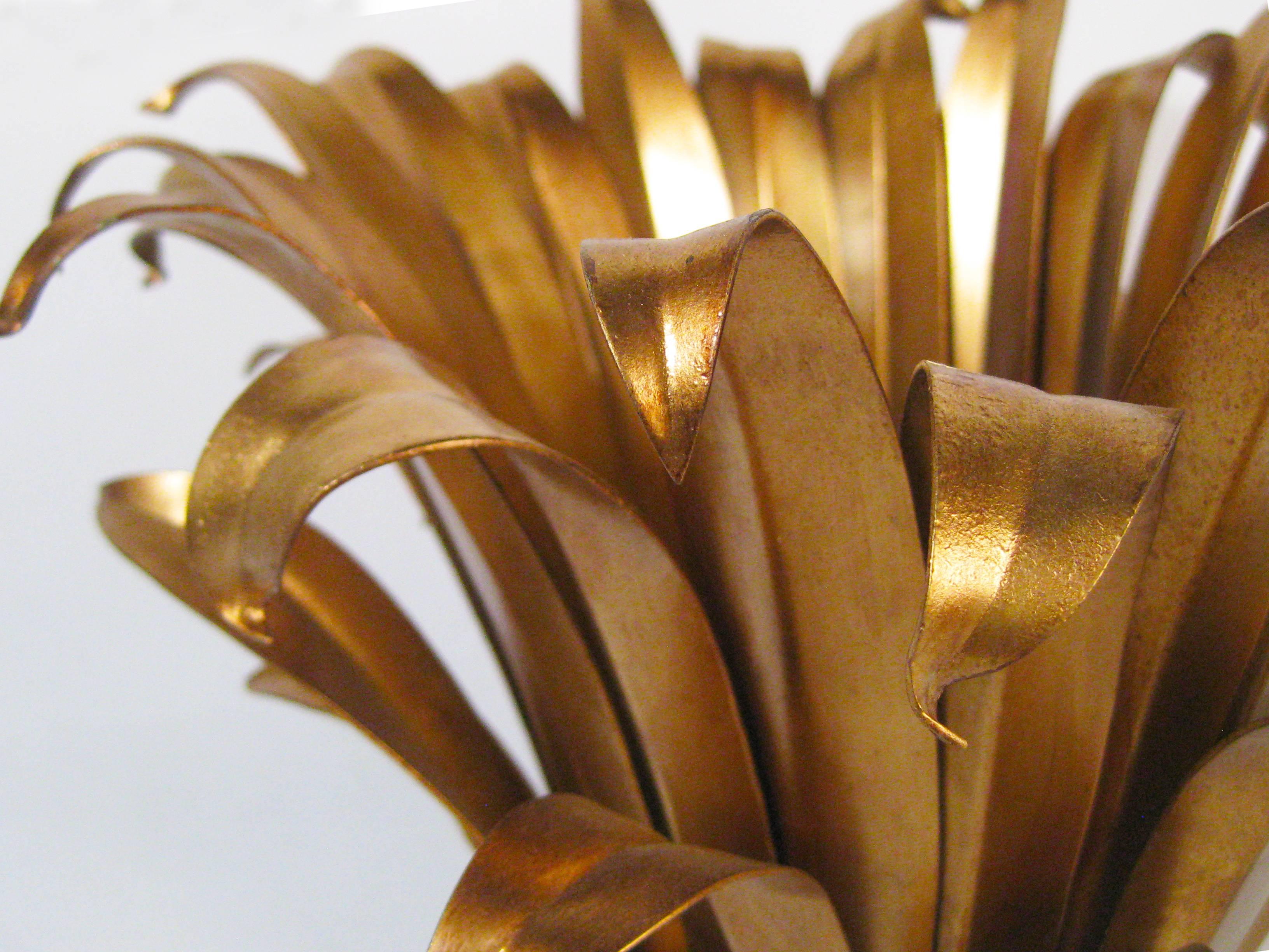 A gilded table lamp of delicately patinated metals that depicts pandanus leaves (or the like!) bound by ribbon. The subtle, textured effect of the light's reflection as it passes out through these layered golden blades is lovely--and pure