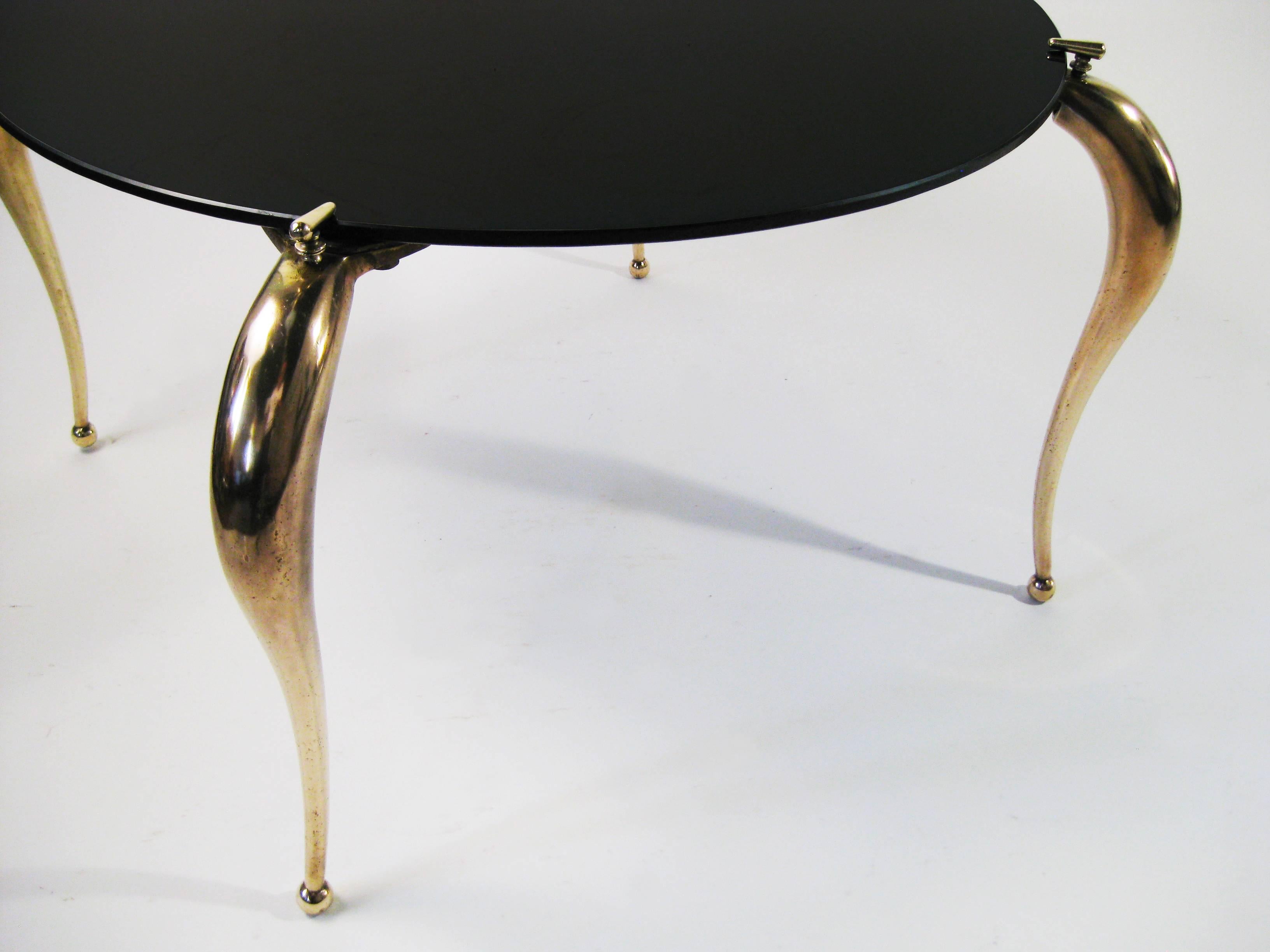 The supple, delicately curved yet formidable bronze legs of this center table support and grasp the original black Carrara glass tabletop as though it were a gemstone, setting the glass with an ingenious clasp on the upper end of each leg. A table