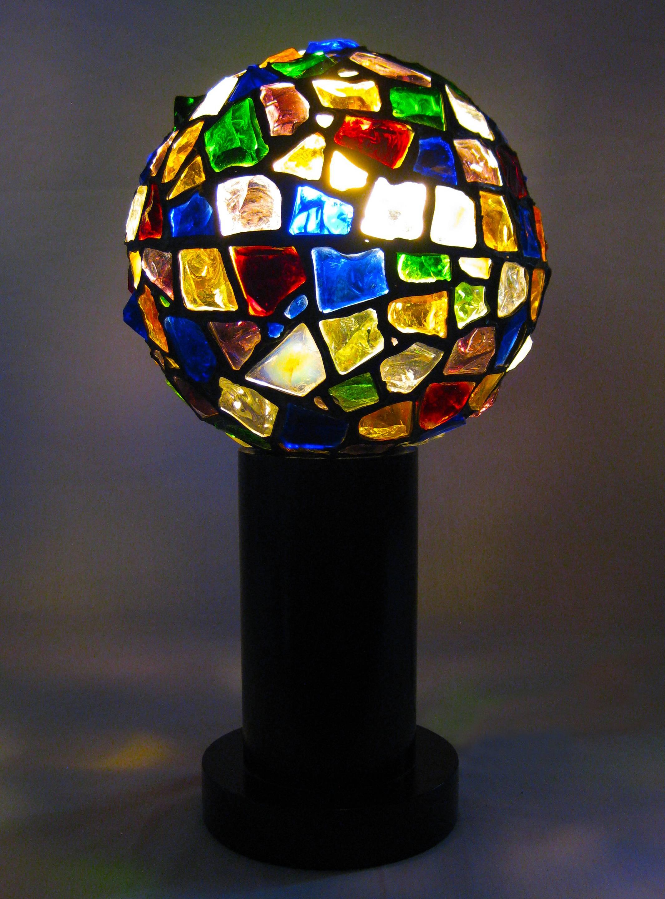 The shade of this table lamp is a rare and beautiful example of the fine art of "emplomado" glasswork in Mexico.  Not simply shards of colored glass--but thick, many-faceted and quite formidable crystals--have here been trimmed and