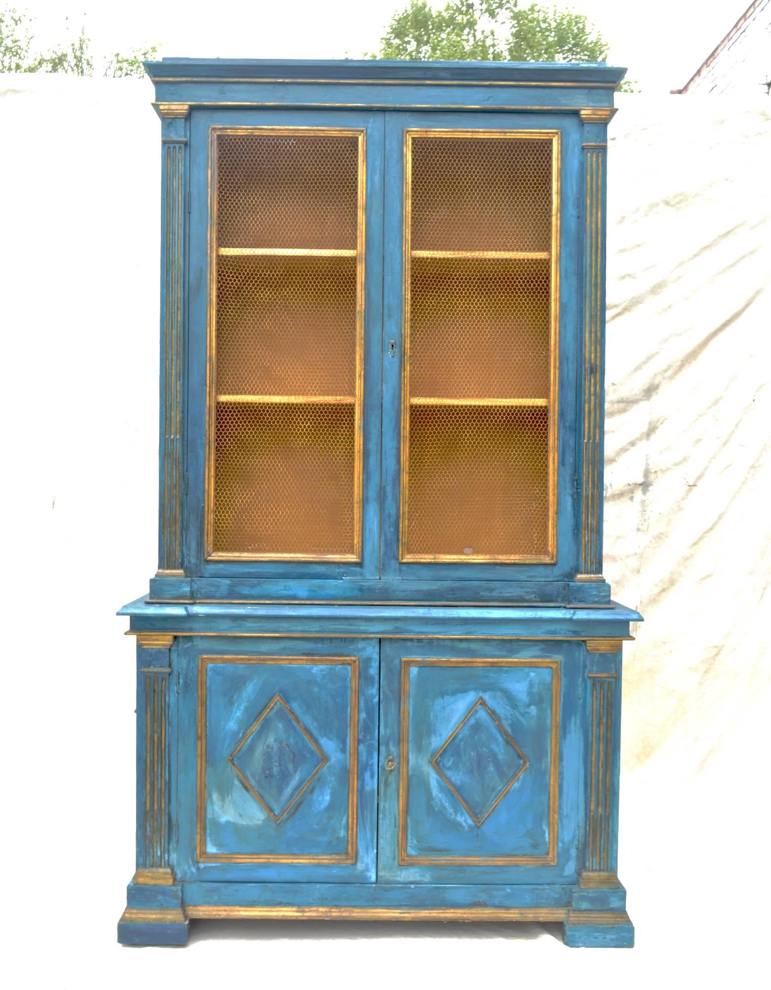 A spectacular mid-20th century Italian two-piece breakfront in striking mediterranean blue plaster. The top having gilt accented moldings, stop-reeded flanking moldings which encase the two large chicken-wired doors which open to reveal a spacious