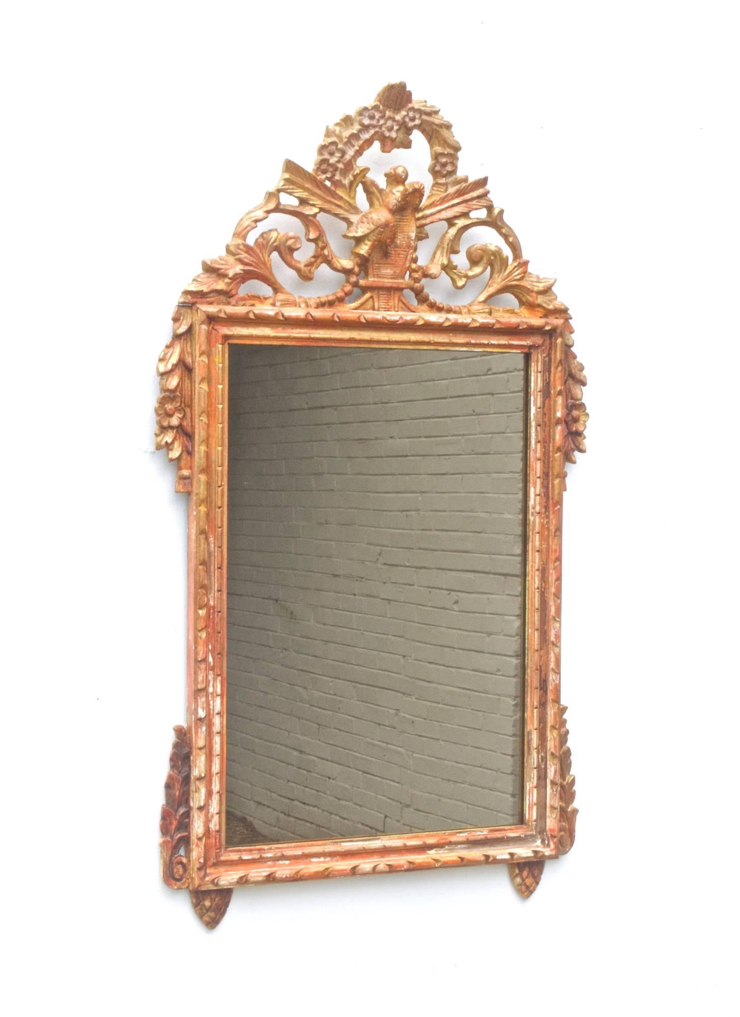 A vintage Louis XVI style looking glass having a weathered and distressed finish. Polychromatic washes of red, yellow, cream and golds mix throughout.