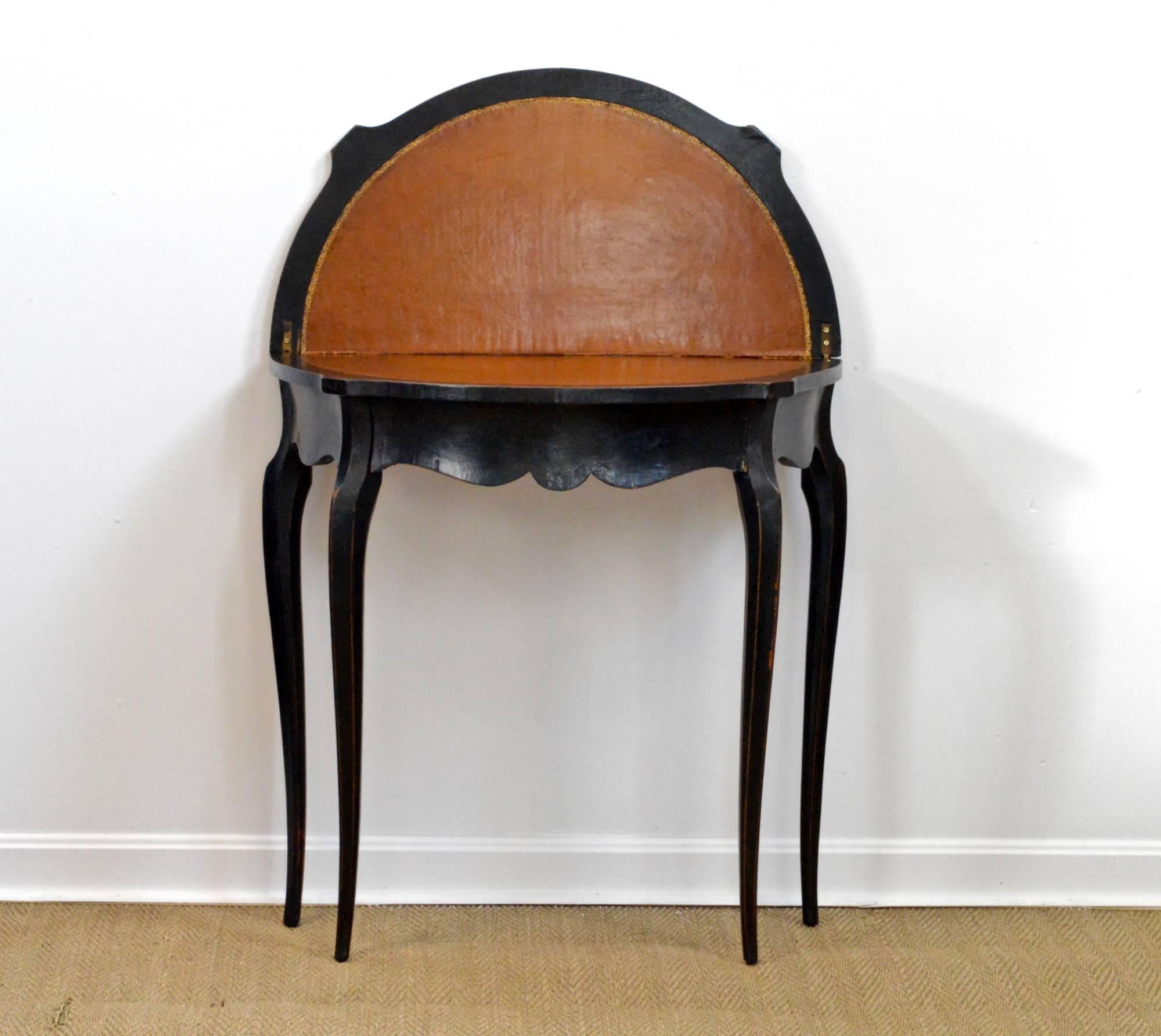 Ebonized Louis XV styled card table of demilune form having a flip-top that opens to reveal a lovely worn leather top which is accented by an embossed outer edge. Rear legs swing behind to supply support to the open game table surface. Wear and