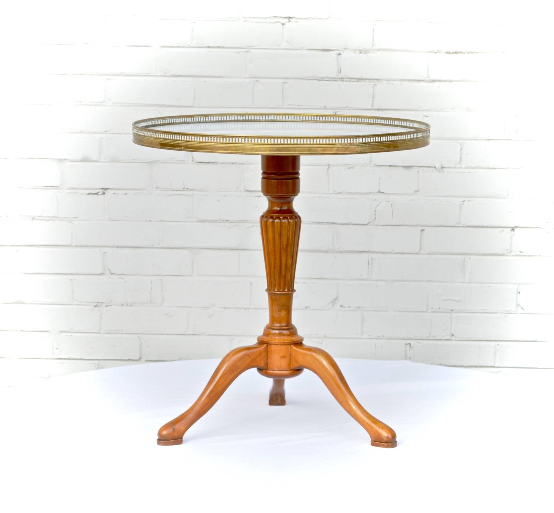 An outstanding gueridon table having a Carrara marble top, encircled by a finely cast brass gallery, which rest upon a tripod base of cherry. The base has a reeded trunk and delicate pad feet. Tabletop and table base are smartly connected by