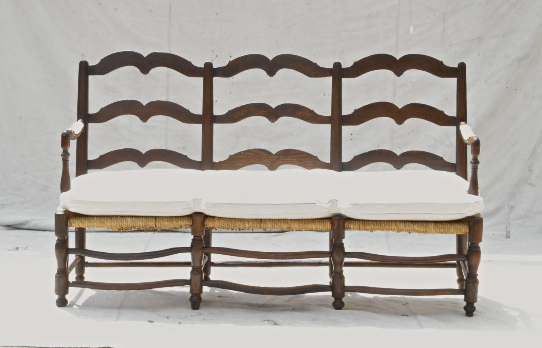 A stylish French Provincial triple back bench in oak. The mid-19th century settee has carved mustache formed back splats, unusual down swept arms that have upholstered armrest trimmed in nailhead, a comfortable down cushion that spans the entire