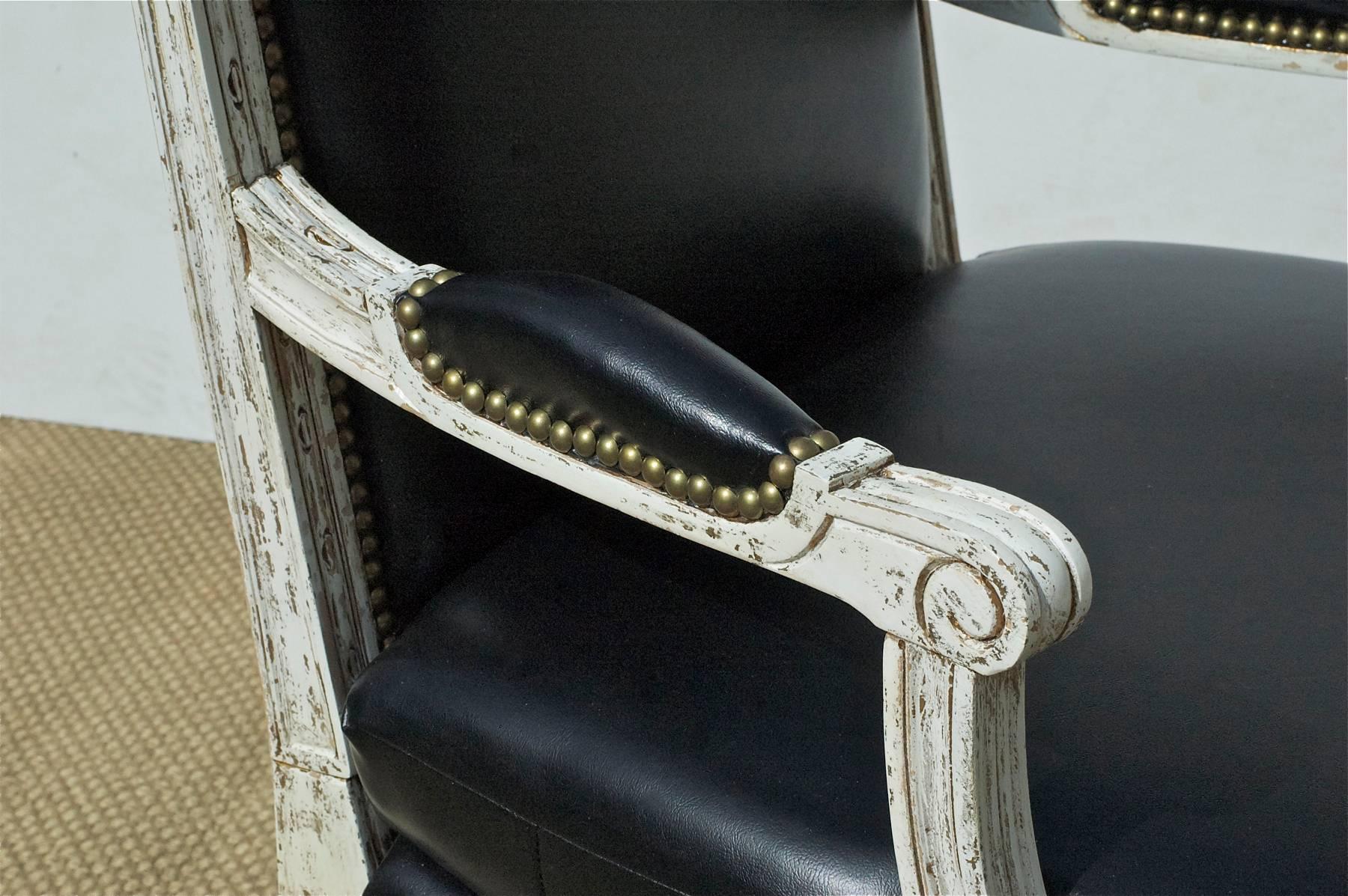 A handsome pair of Louis XVI style bergere in a recent dry scraped finish and black leather with fetching brass nailhead trim throughout. The simple and timeless lines of these chairs allow them to be easily employed within a modern interior.