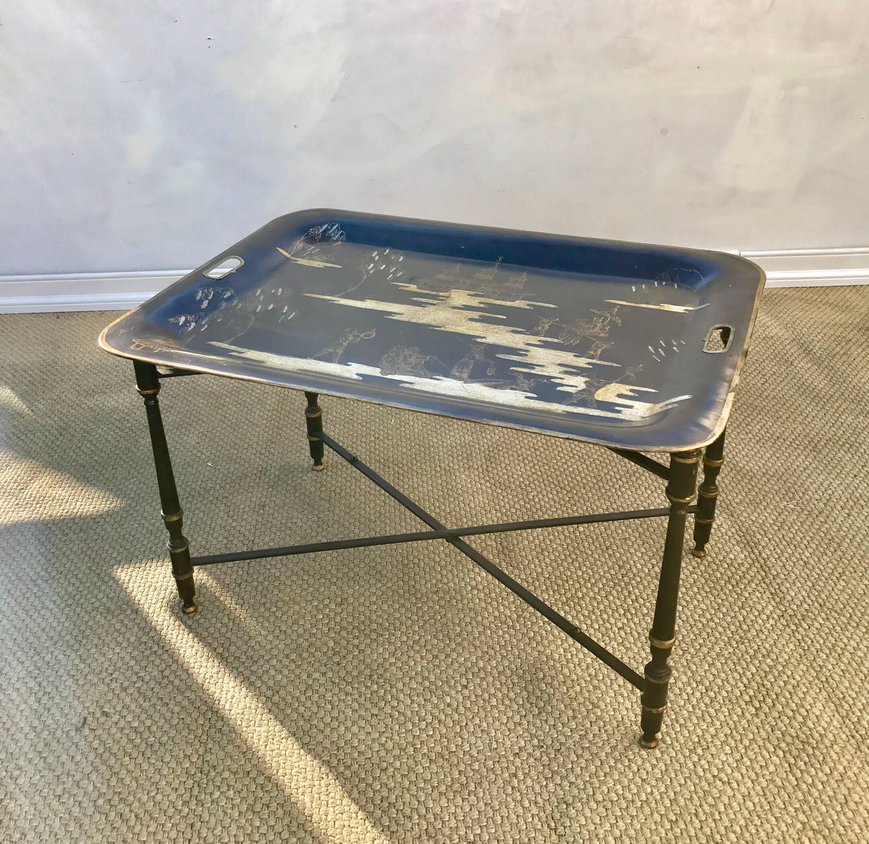 An Italian made tole painted tray on stand as coffee or cocktail table. The chinoiserie styled paintwork on the tray depicts a whimsical village at work and play. The dark bridle brown and gilt paint work on the base gives this table added richness.