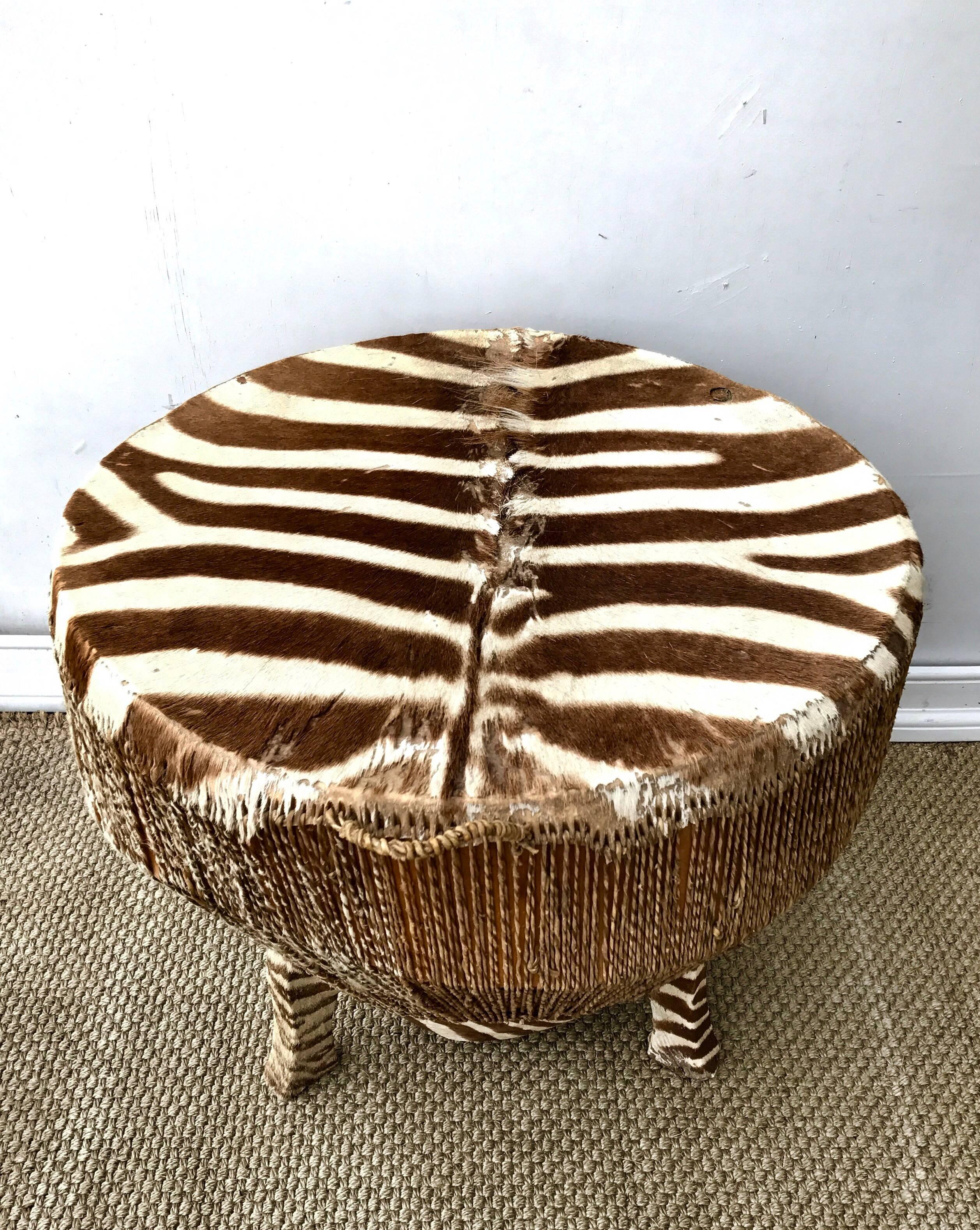 A mid 20th Century African drum table of carved hardwood and stretched zebra hide. The look is organic and natural, global and bohemian inspired. All three feet are wrapped in zebra hide which certainly gives this interesting side table quite a