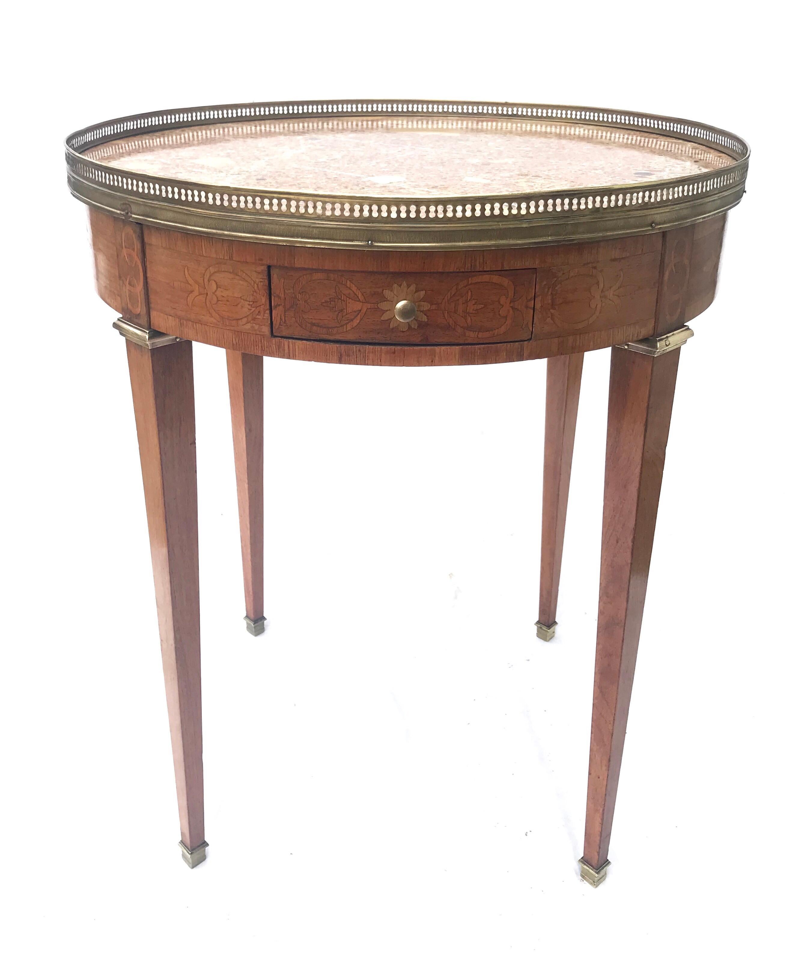 A glamorous French bouillotte table having a polychromatic breche' marble top circa 1930, having flowing and simple inlay work all around the dual drawered and dual slidered table apron. Tall and sleek legs of light mahogany terminate on classical