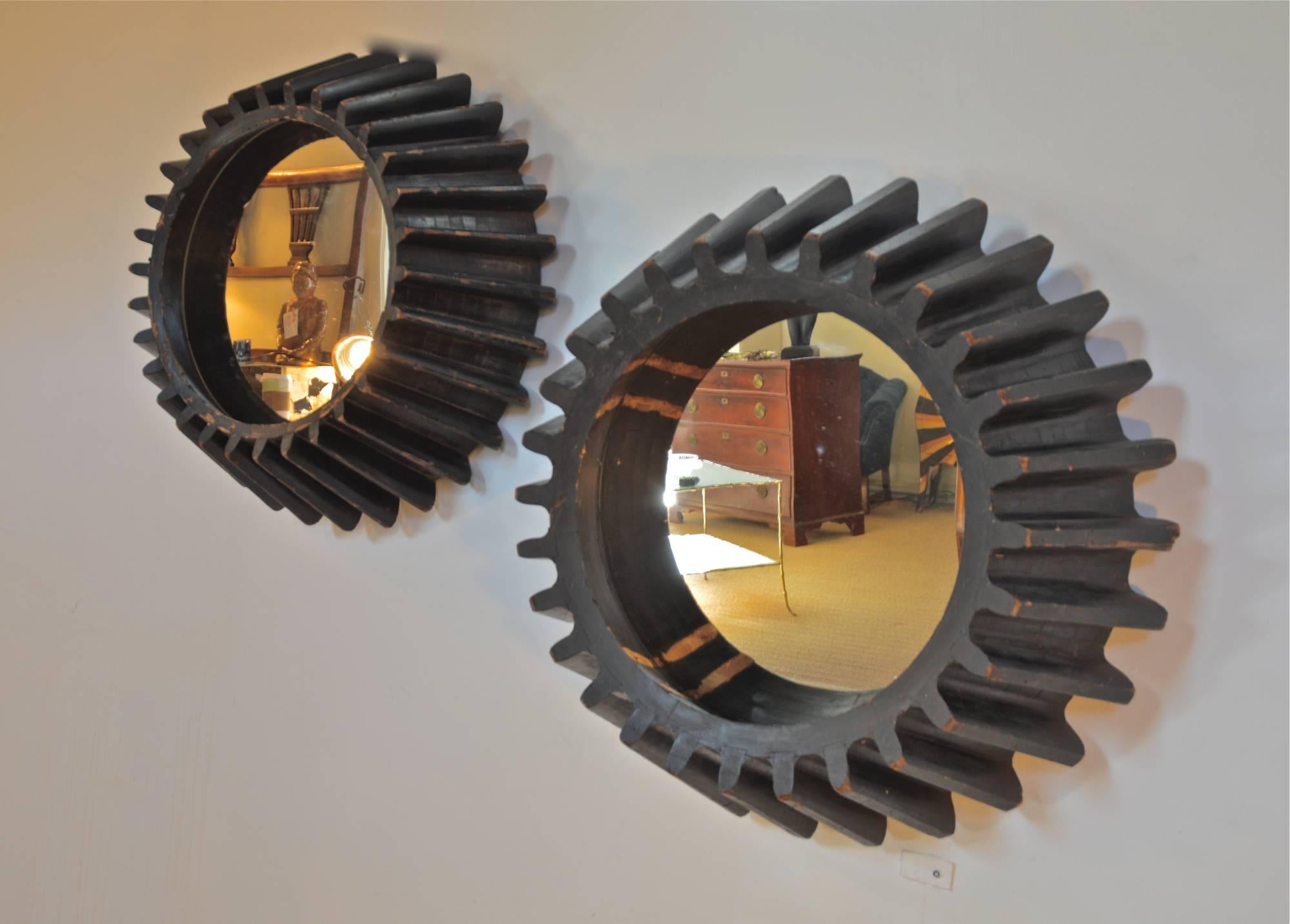 A near pair of Industrial cog-wheel foundry molds which have been cleverly re-defined as wall-mounted mirrors. Striking architectural detail and a unique geometry make these factory-chic reflectors useful in a myriad of locations. 
One cog-wheel