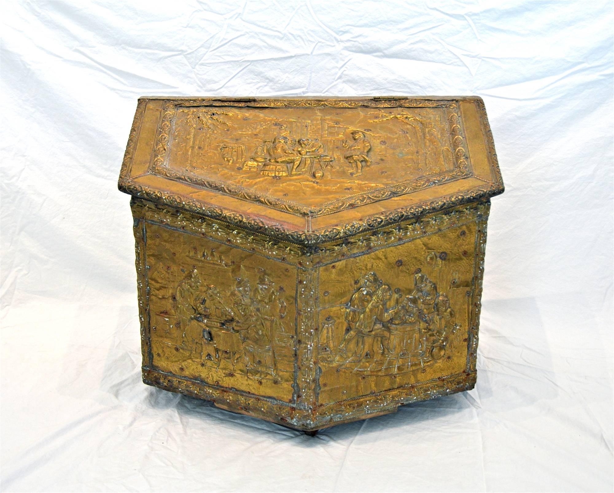 Early 20th Century firewood box of brass and pine. The box of trapezoidal shape, is crafted of repoussé brass sheet and depicts various groups of jovial men having a good time. The hinged top is adorned with a wonderful egg and dart trim moulding.