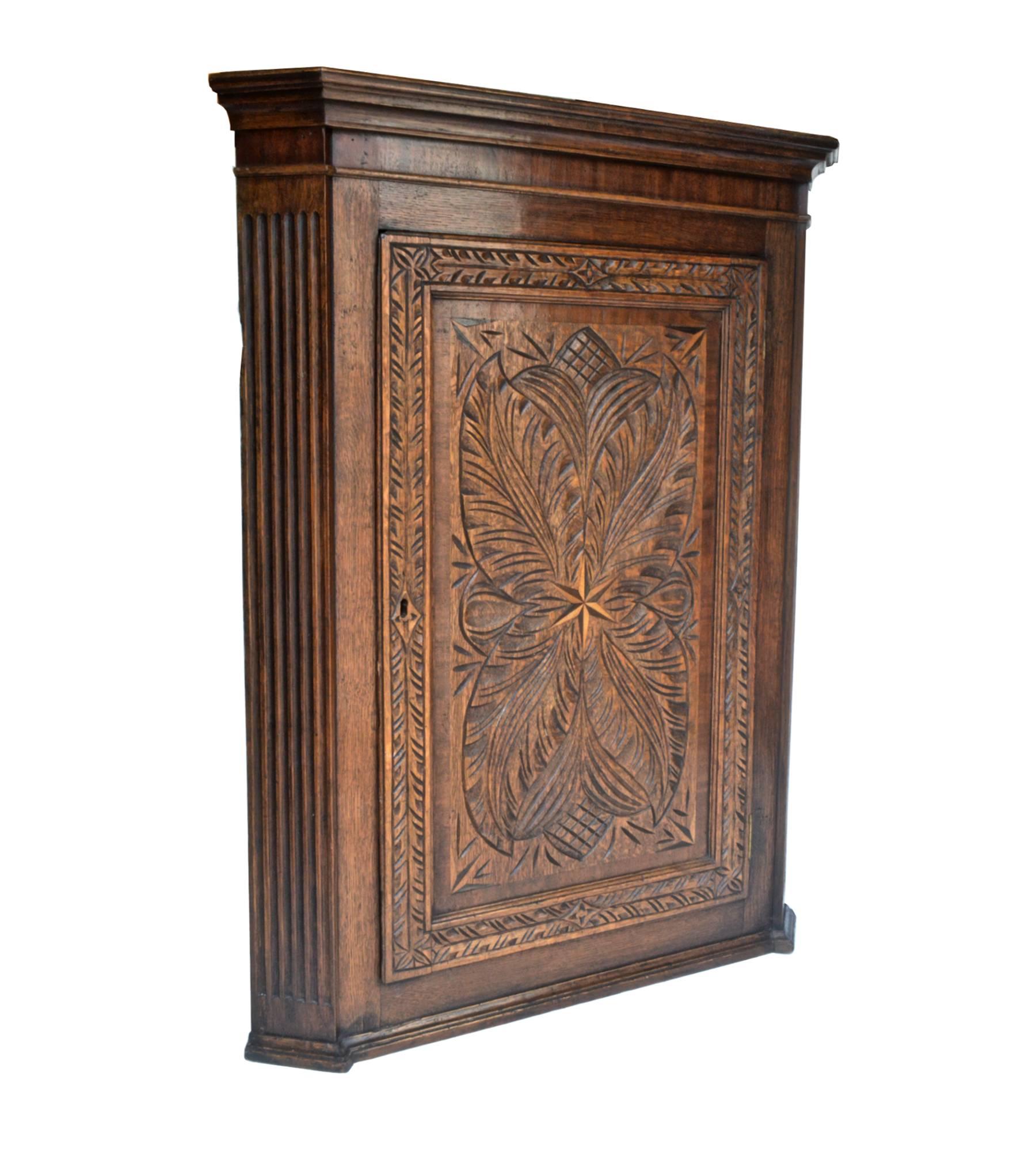 19th century corner cabinet of oak. The hanging cupboard has a glorious hand-carved blind and hinged swinging door that opens to reveal three ample shelves of sound storage. The rich and natural patina of the cabinet will warm up any room in which