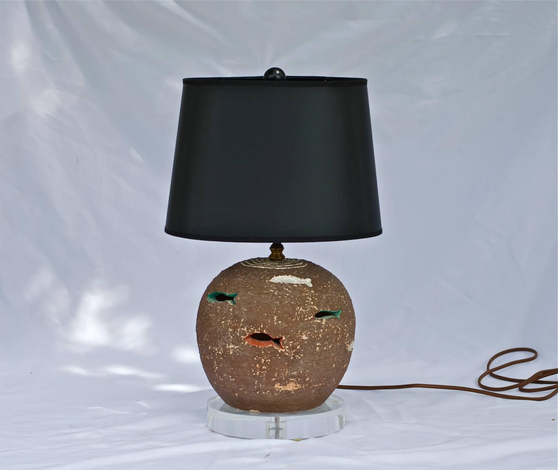 A whimsical pottery lamp with fish throughout the surface. The piece was signed, yet at some point the makers mark was chipped off as noted in photography. Recently added custom Lucite riser and new high quality brown cloth wrapped lamp cord. The
