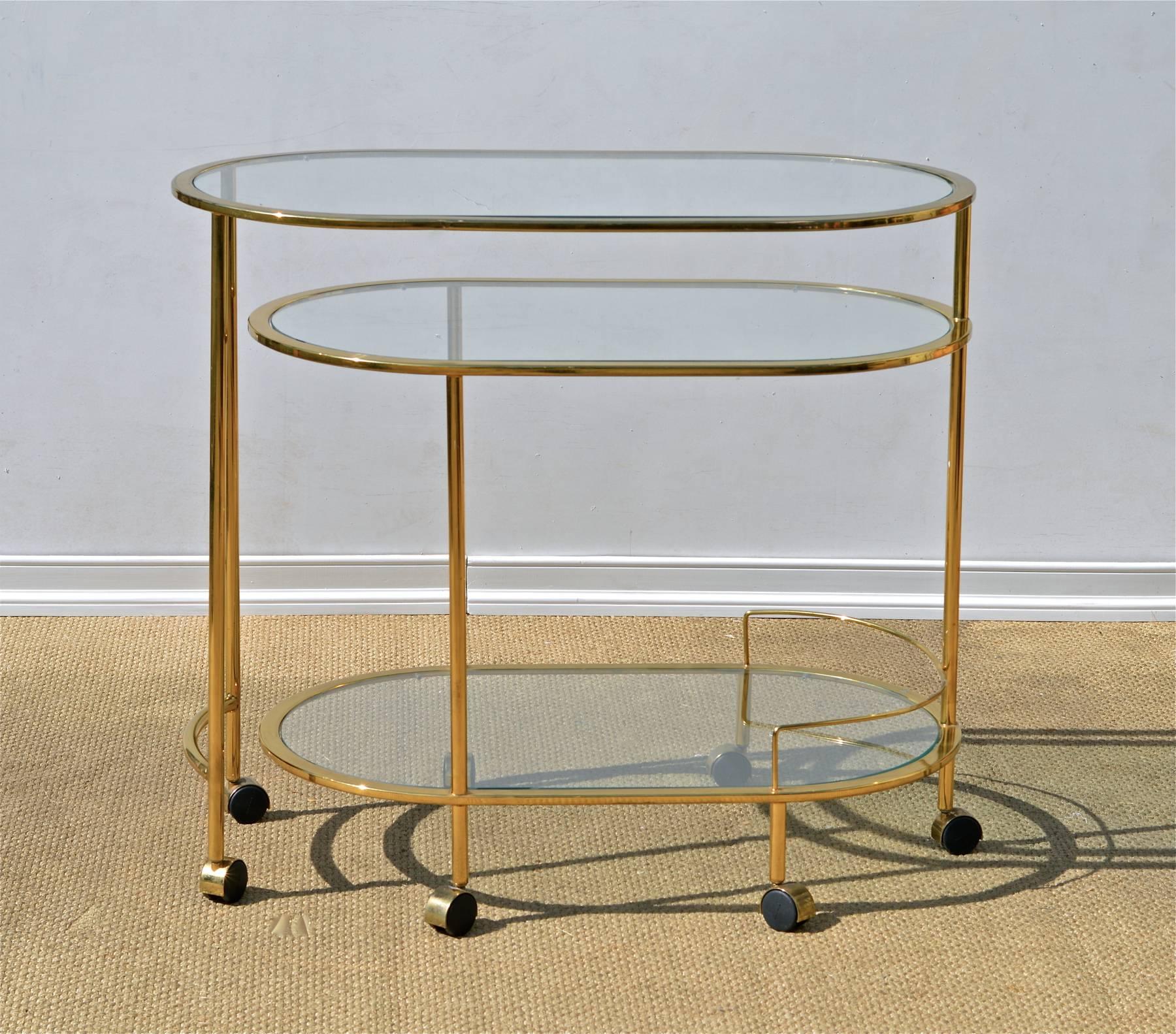 Vintage bar cart of brass and glass in the manner of Karl Springer. The functional service trolley articulates 180 degrees to provide maximum surface area for entertaining.