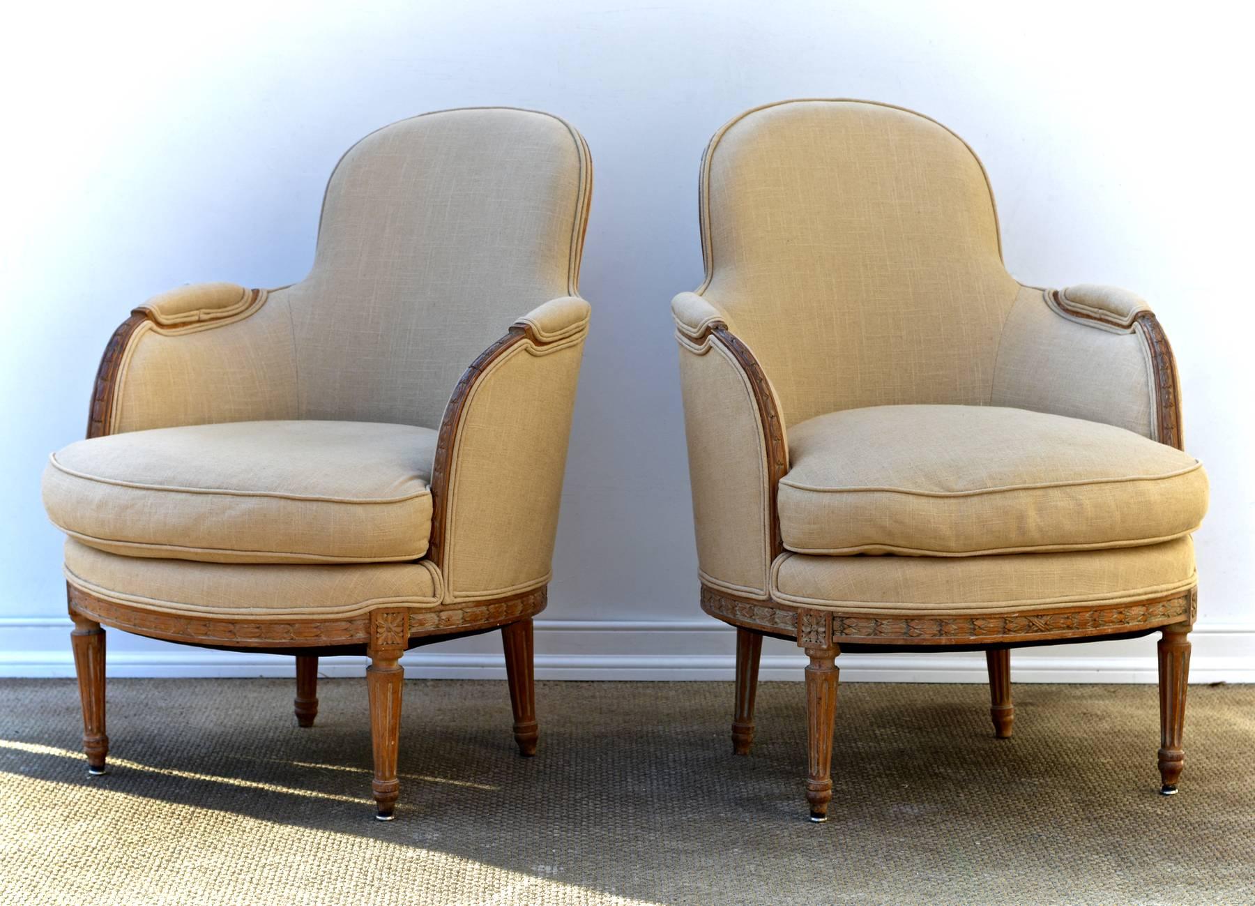 A sumptuous pair of Louis XVI style bergere chairs dressed in a supple and stunning Calvin Klein linen. The hand-carved, early 20th century chairs are tight and sit like a dream. The frames are gently pickled and show faint traces of original paint