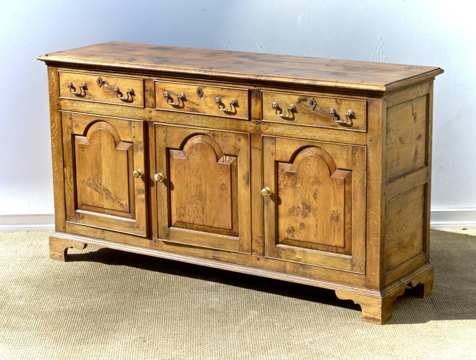 An attractive and narrow Welsh dresser base in the late 18th century style. The vintage 1970 buffet has a slender and ogee edged top resting on three ample sized drawers that reside above an open storage cabinet that is adorned with three tombstone