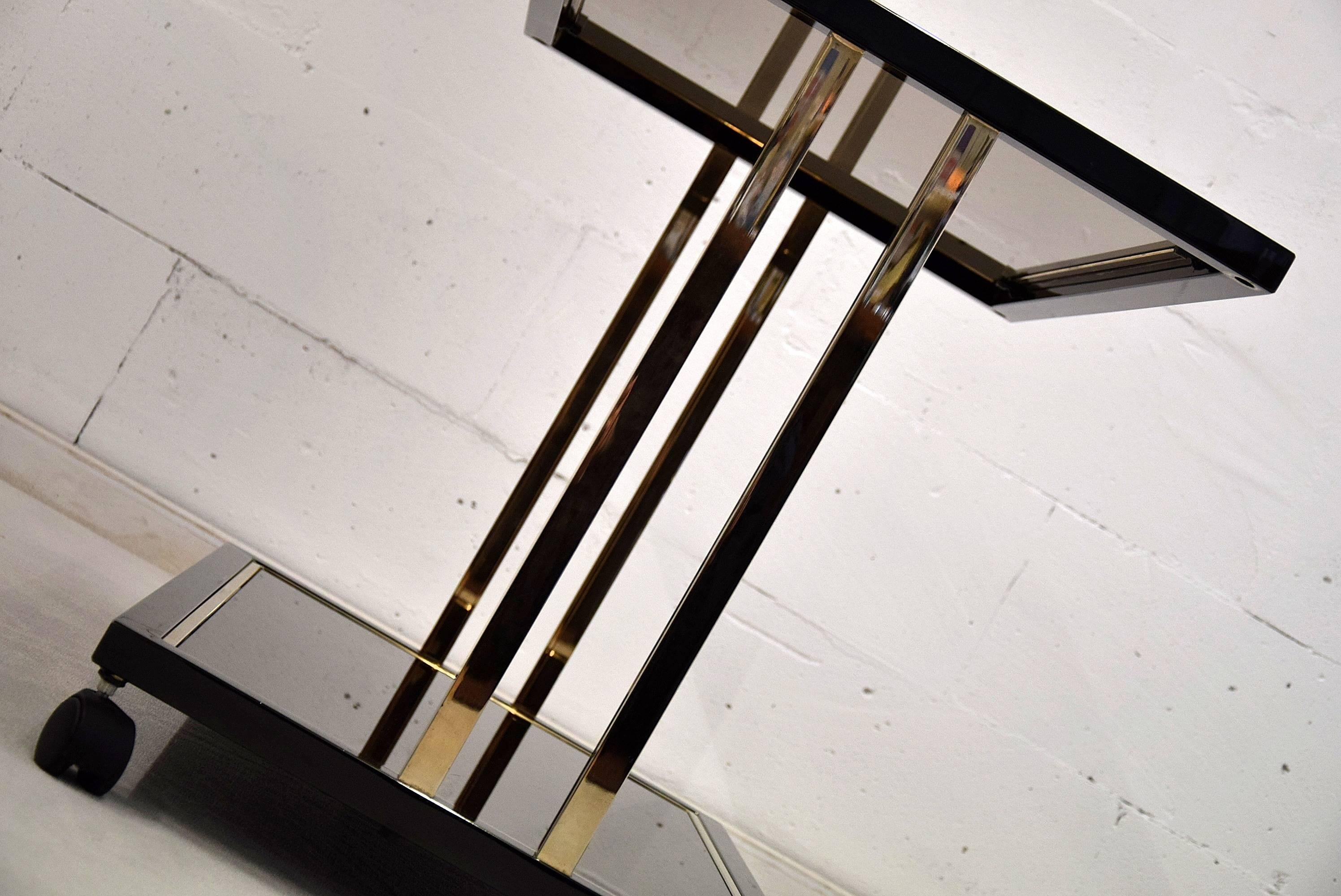 Two-tier Mid-century modern Belgo chrome serving table
Stylish 23-carat gold plated two tier serving table or bar cart produced by Belgo Chrome in the 1980s.

The top has fume smoked glass and the bottom tier bronze mirrored glass with a small