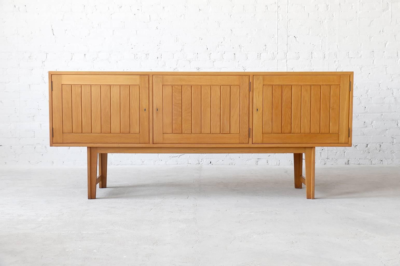 A fine white oak sideboard by Kurt Østervig for Vamo Sonderborg. Excellent construction techniques and the use of large amounts of solid oak including the doors, drawers, frame and legs. Three storage sections including two felt lined drawers. 

-