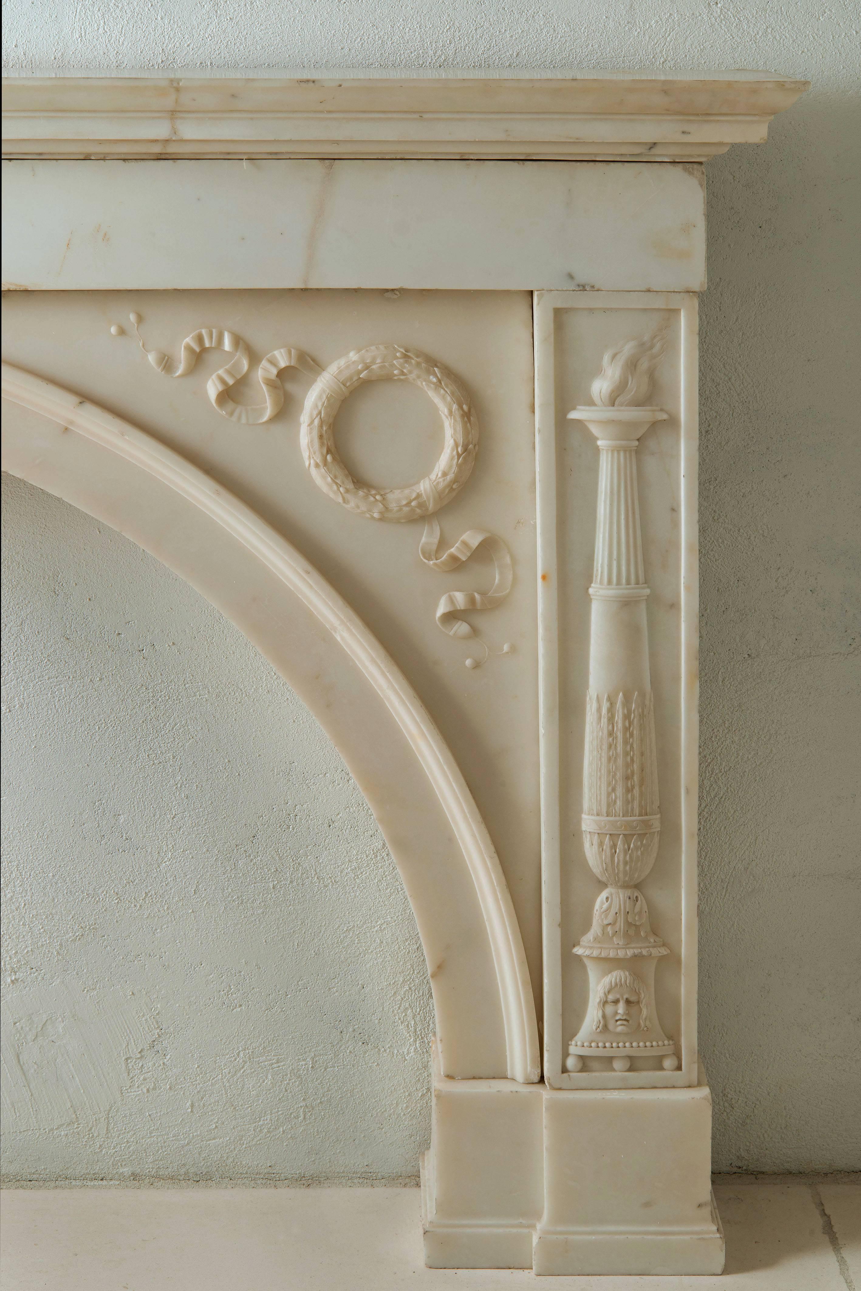 This beautiful white marble fireplace is attributed to Thomas Hope (1770-1831).
The marble is carved with a Gorgon head in the centre and crowns on both side of the inside, two torches on the entire height of its jambs.
 