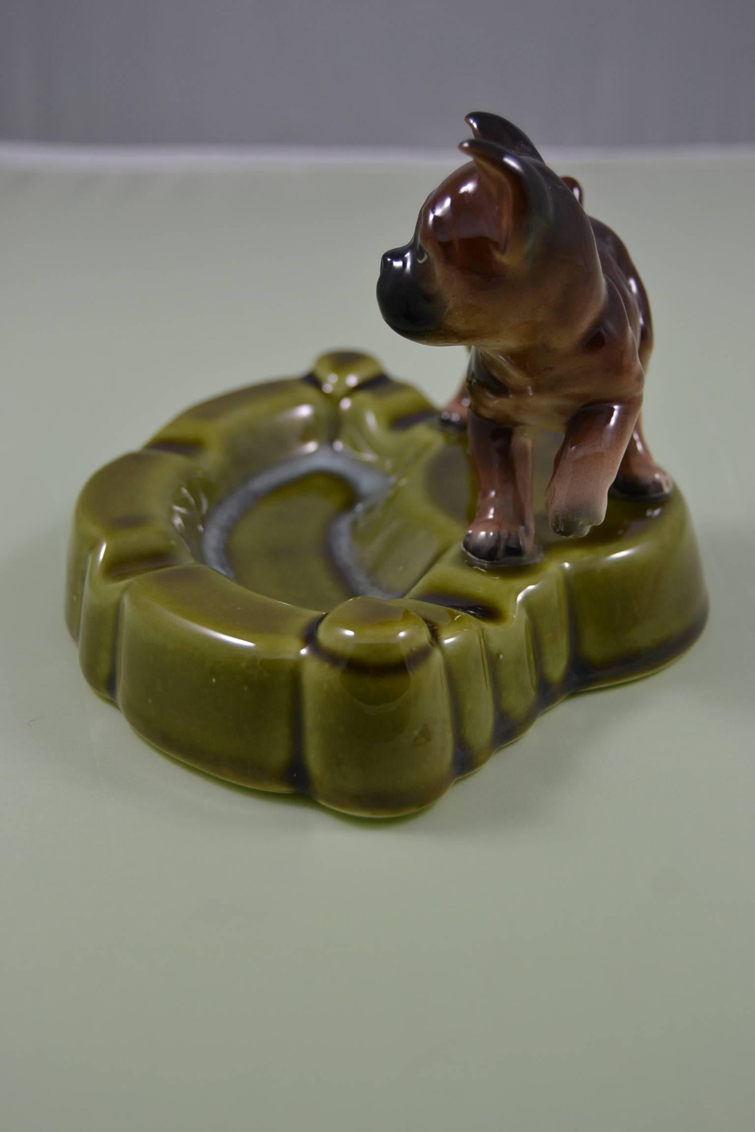 Vintage ashtray with dog from the Mid-20th Century. 
A green porcelain ashtray with a puppy dog on top. A brown with black masked dog.
This ashtray was made in Japan. 

Beautiful gift for a Dog lover. 