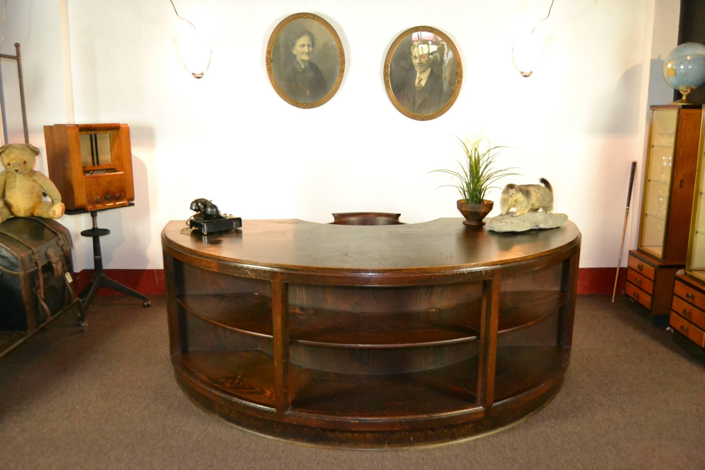 Impressive half round wooden executive desk.
Antique handmade Art Deco desk from the 1940s.
Used condition, what gives a beautiful old patina.
In front with open shelves so you can expose items, books at the back also storage place left and