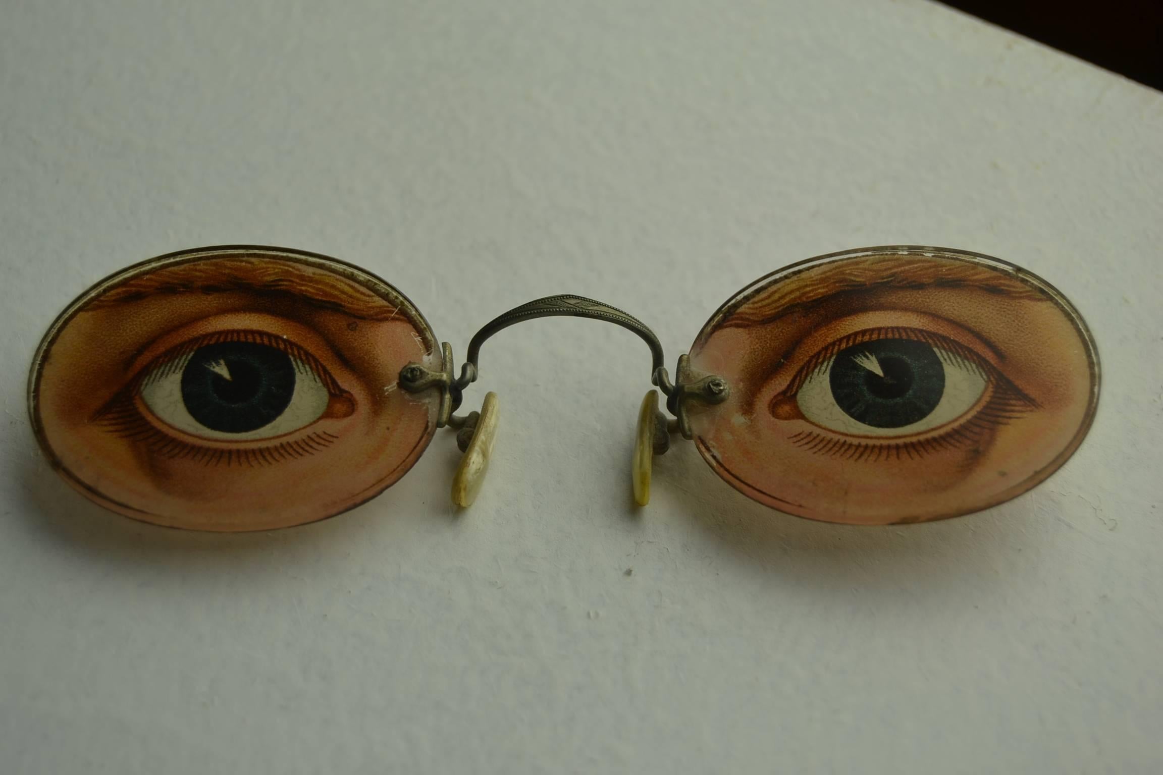 Unique pince-nez / pinch nose spectacle from the early 20th century.
Hard metal silver tone bridge with nose clips of mother-of-pearl.
Rare glasses with vintage image illustration of human eyes.
Miniature optical sign optometrist sign