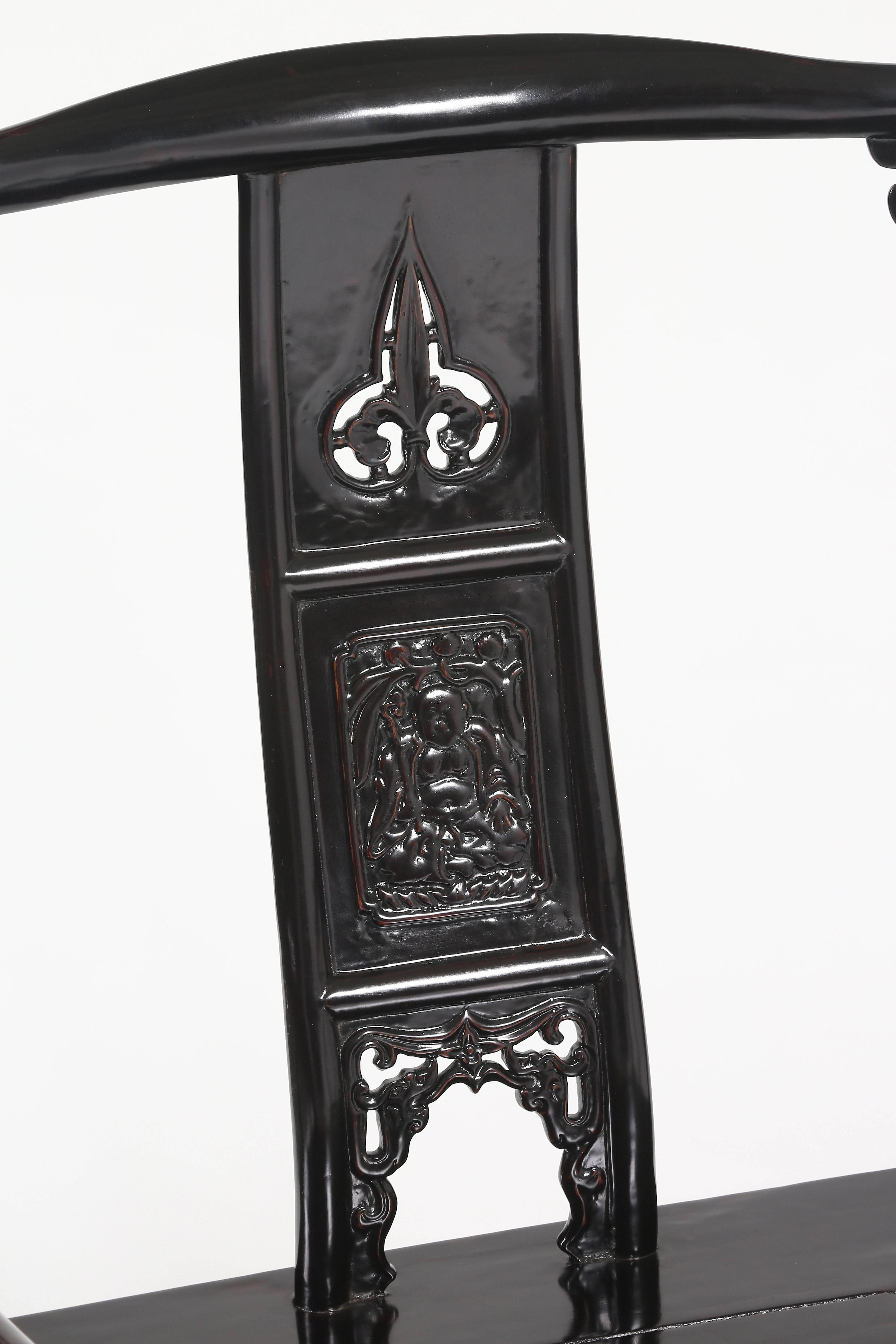 The shaped top rail supported on the side posts, decorated with carved cusped flanges, a S-curve back splat decorated in three sections, the top section open-carved with ruyi motif, the middle relief carved with a seated Buddha in mirror images on