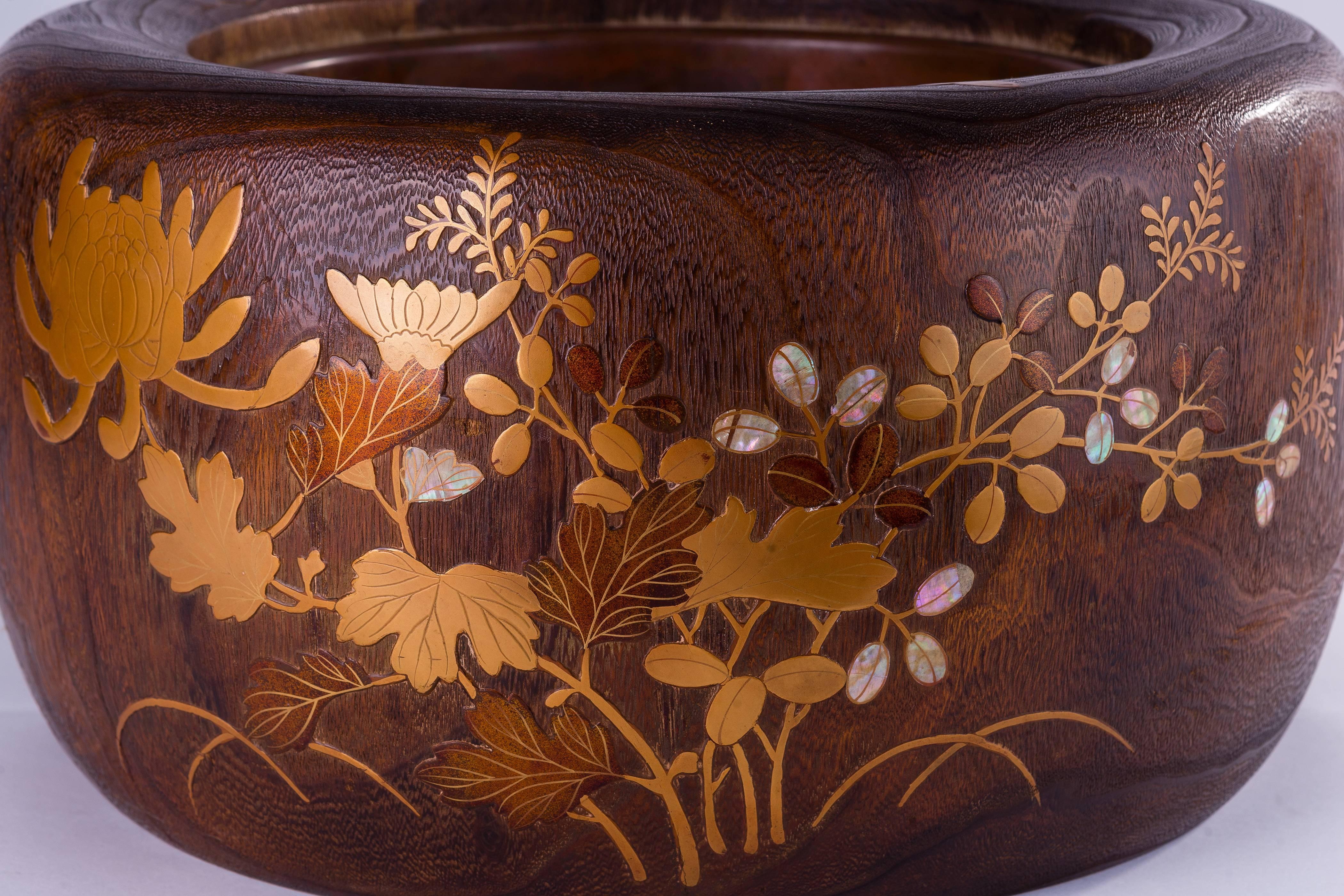 The Japanese hibachi (fire bowl) is handcrafted in wood, finely decorated with chrysanthemum and foliage, and executed meticulously in hand-worked lacquer work with brass and mother-of-pearl inlay. 
The circular hibachi lined with a brass container