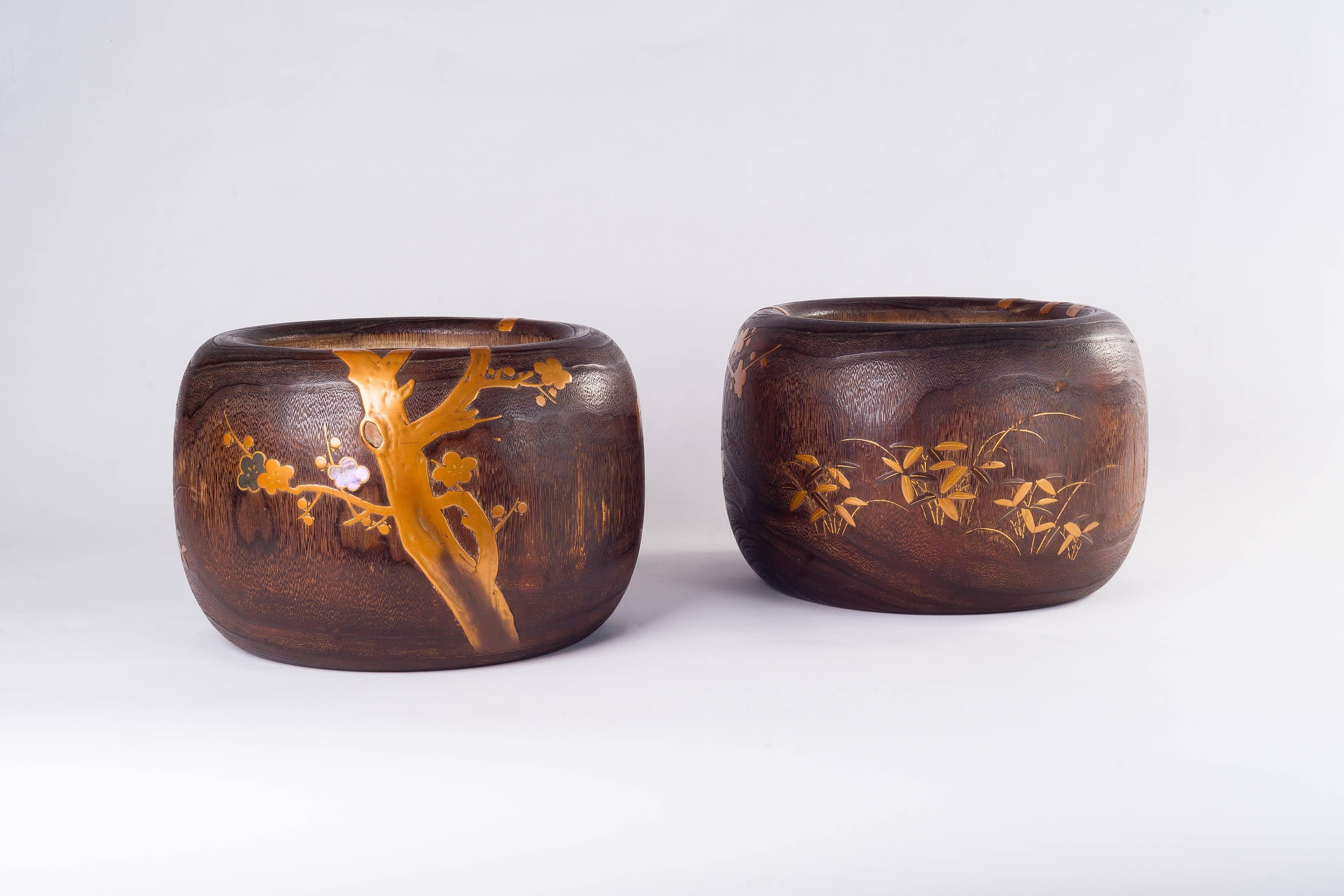 The hand-crafted pair of Japanese wooden hibachi (fire bowl) is finely decorated with plum blossom tree and foliage, and executed meticulously in hand-worked maki gold lacquer work with brass and mother-of-pearl inlay. The circular hibachi lined