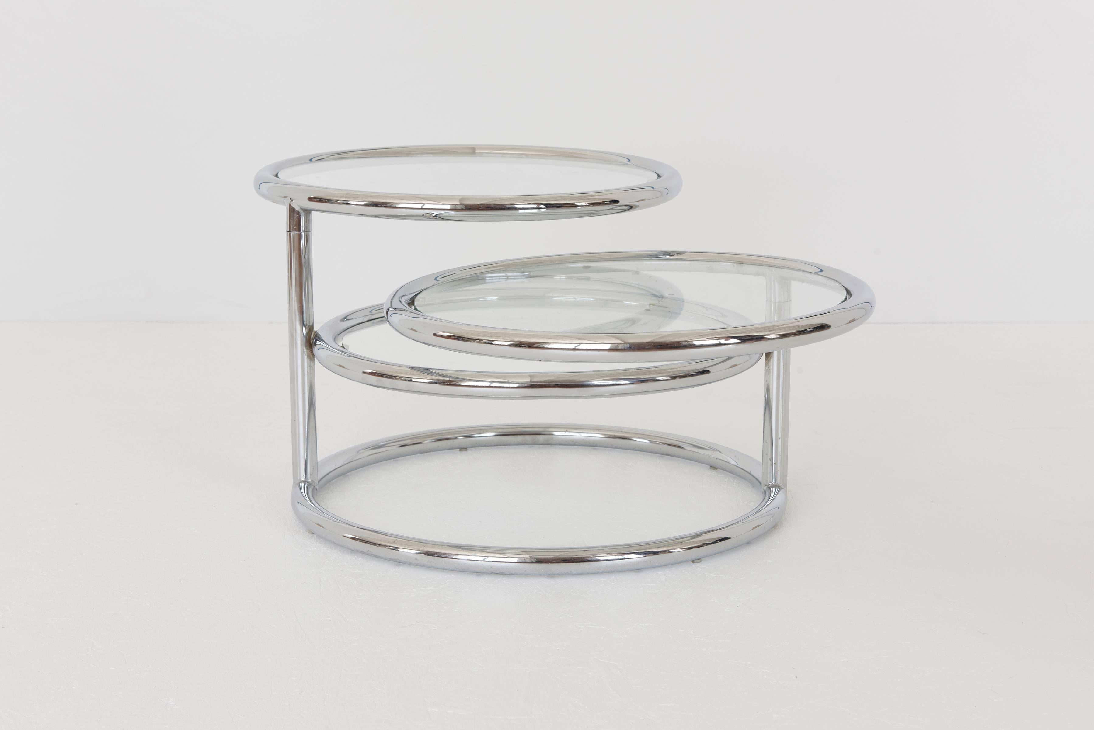 Adjustable multi-tier coffee table with two circular sections that swivel out to extend the table. Table is comprised of tubular chrome-plated metal frame and clear glass tops (3 surfaces). Table extends to 66 in. wide.