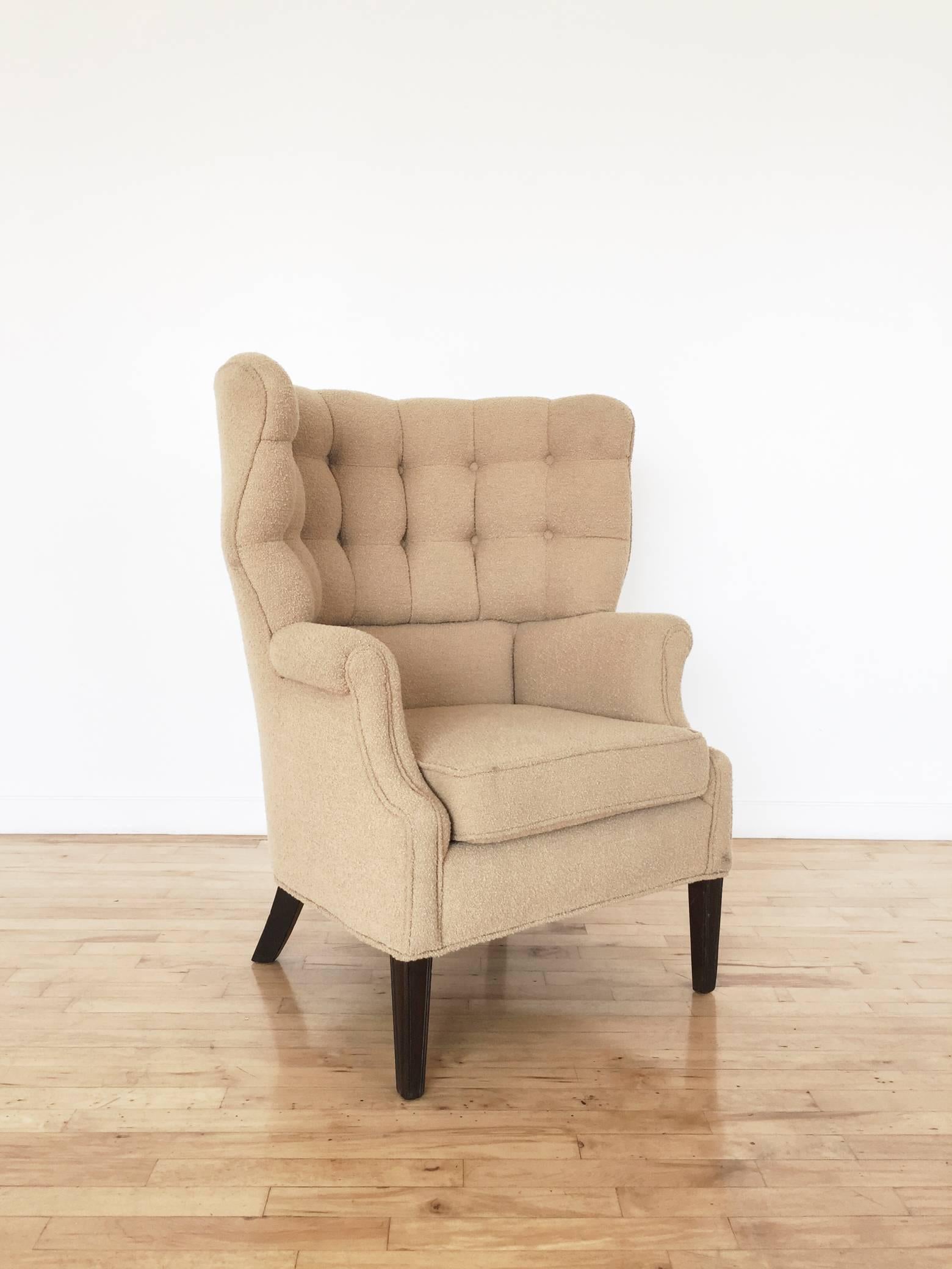 Modernist wing chair with tufted, curved high back and scrolled arms. Upholstered frame sits on dark wood legs. Upholstered in tan wool bouclé that remains in very good condition. A Mid-Century take on the traditional English club chair.