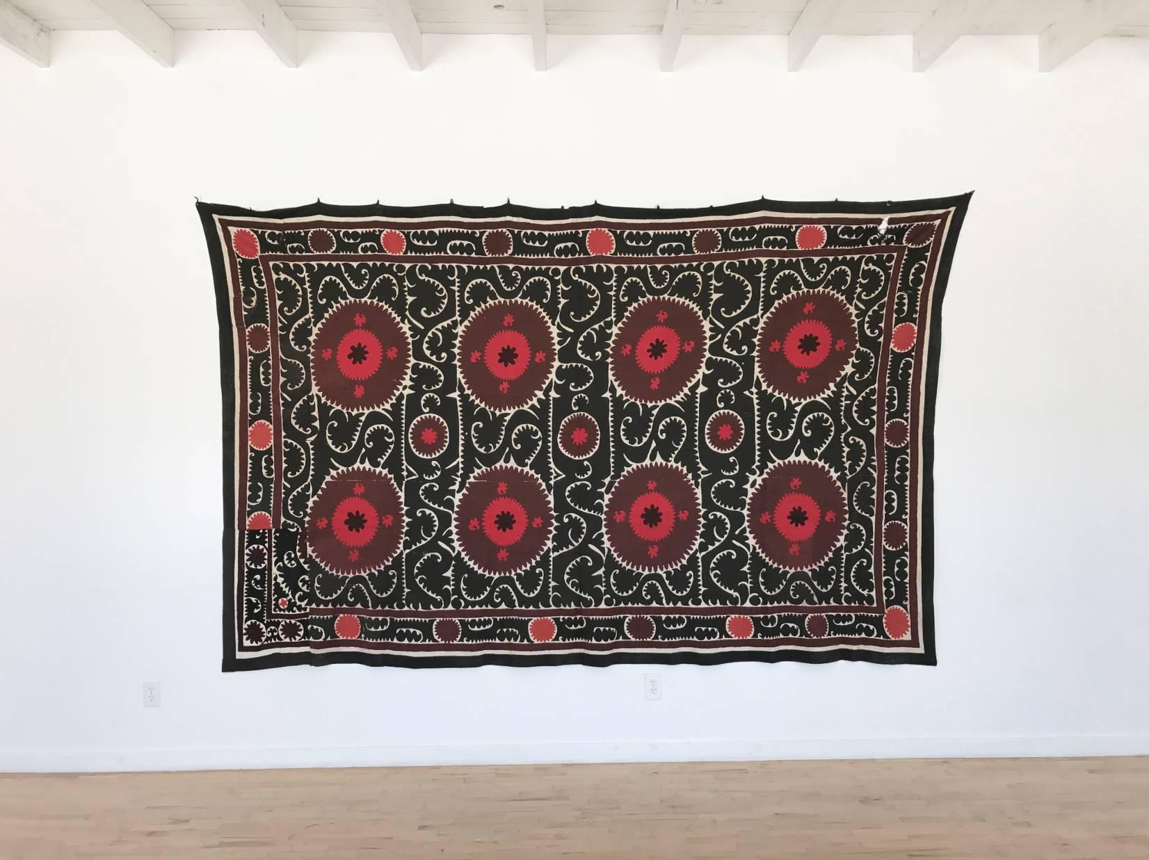 Intricate hand-embroidered needlework Uzbek Suzani with black background and red, maroon/brown and white geometric and paisley motifs throughout. Linen and cotton with silk threading. Very large size can act as a bold wall hanging, bedspread or sofa