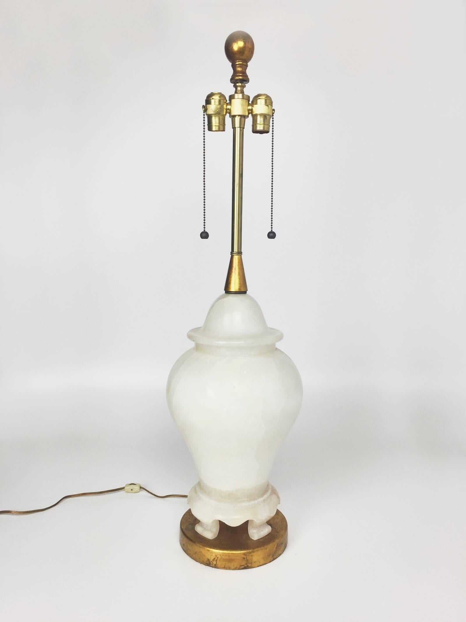 Oversized Mid-Century Modern carved alabaster table lamp in footed urn form, set atop a giltwood base by The Marbro Lamp Company. Double fitting for two bulbs. Matching gilt finial. Brass detailing. Alabaster element likely sourced from