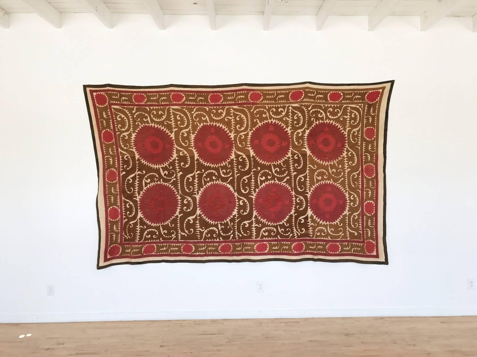 Intricate hand-embroidered needlework Uzbek Suzani on cream background with beige, red and pink geometric and paisley motifs throughout. Beige border. Linen and cotton with silk threading. Very large size - can act as a bold wall hanging, bedspread