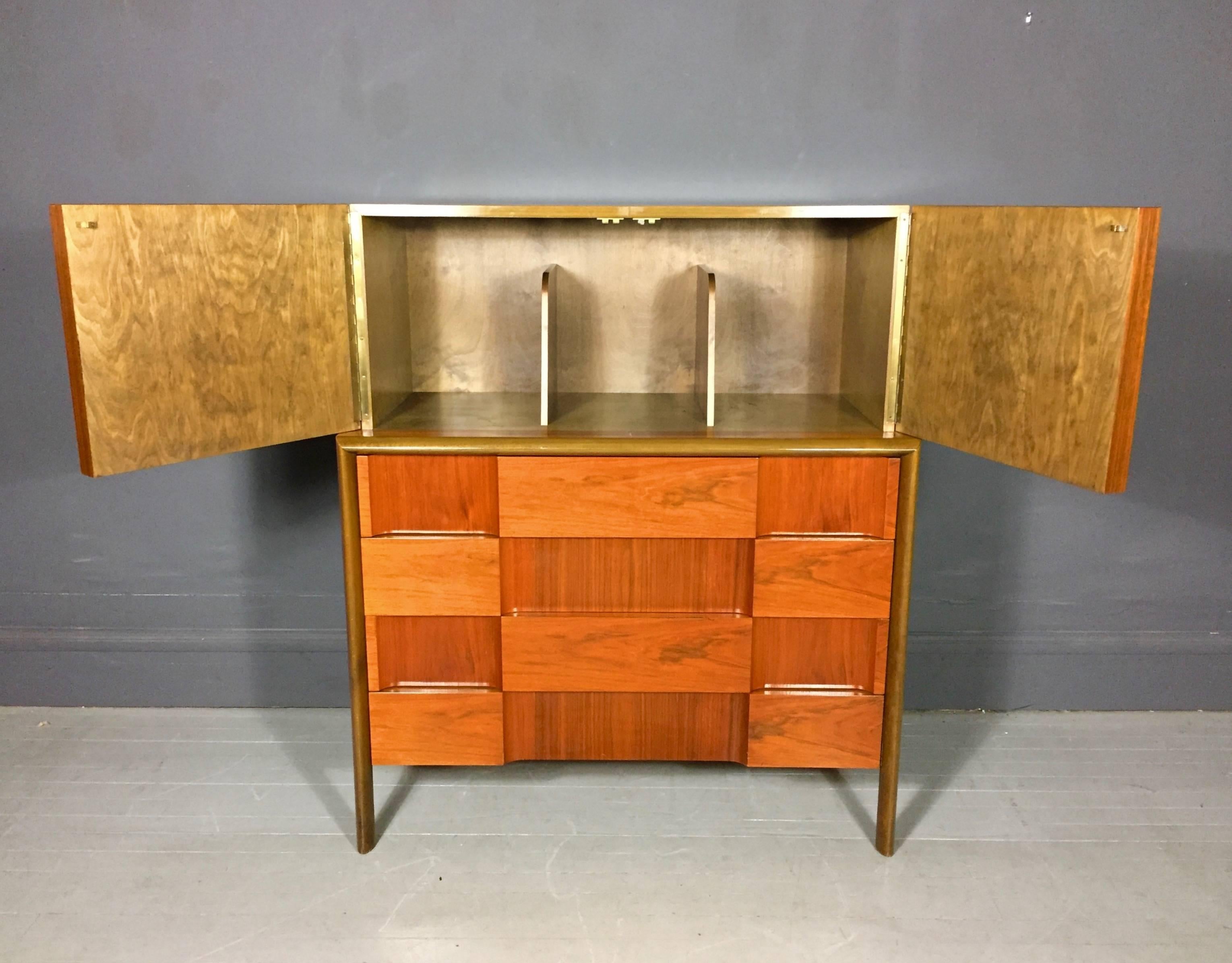 Beautiful and architectural tall chest in alternating geometric walnut veneers, four lower drawers and a top cabinet with two doors, base is accented by carved beech trim. Edmond J. Spence, Sweden, 1950s.

Minor veneer loss to top of one drawer