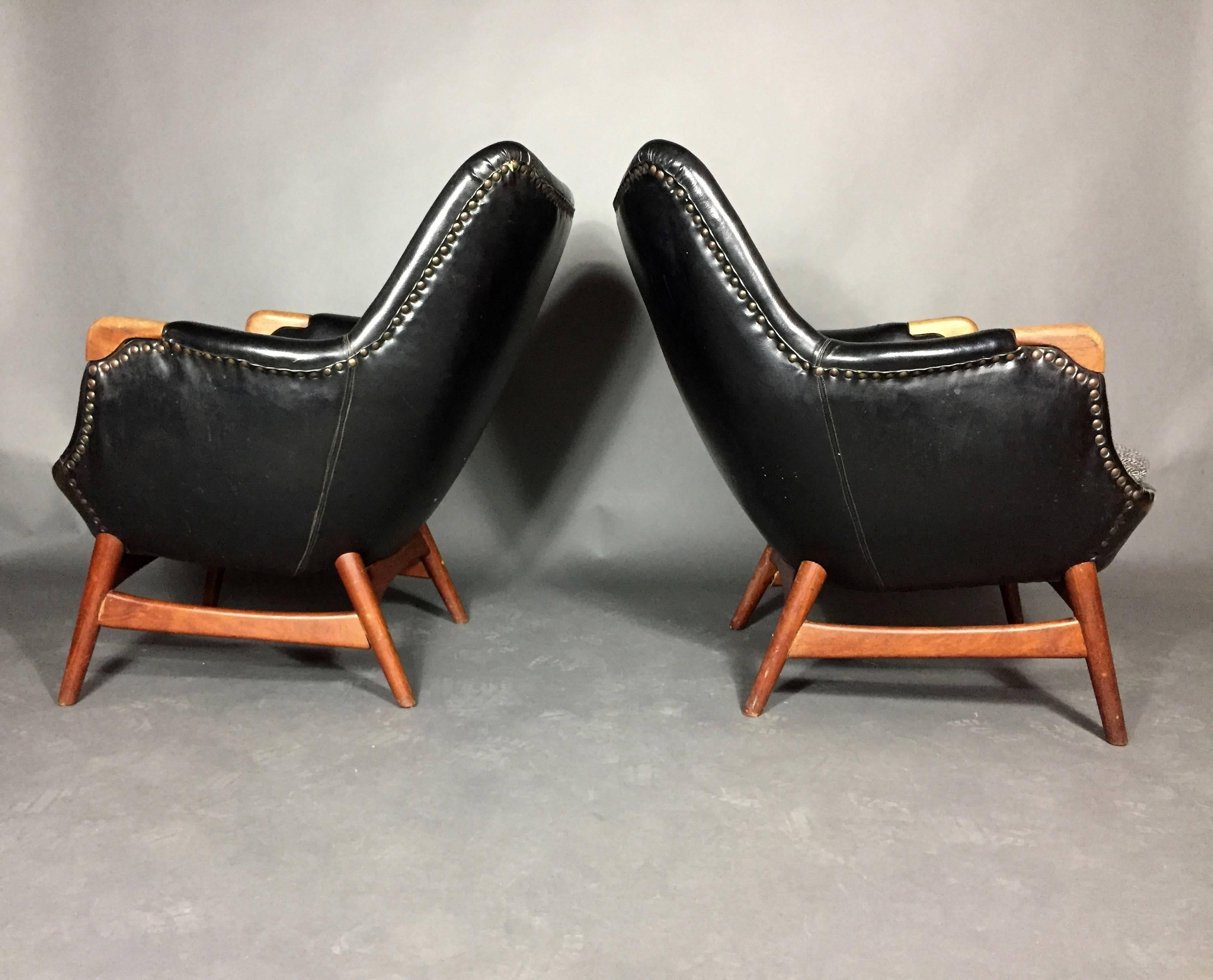A rare pair of beautifully sculpted lounge chairs in black buttoned-back Naugahyde with brass tacks over teak frame. Carved teak armrest tips. Designed in 1956 by Erling Torvits. Denmark. Unmarked.

Some indentations to Naugahyde at back, repaired