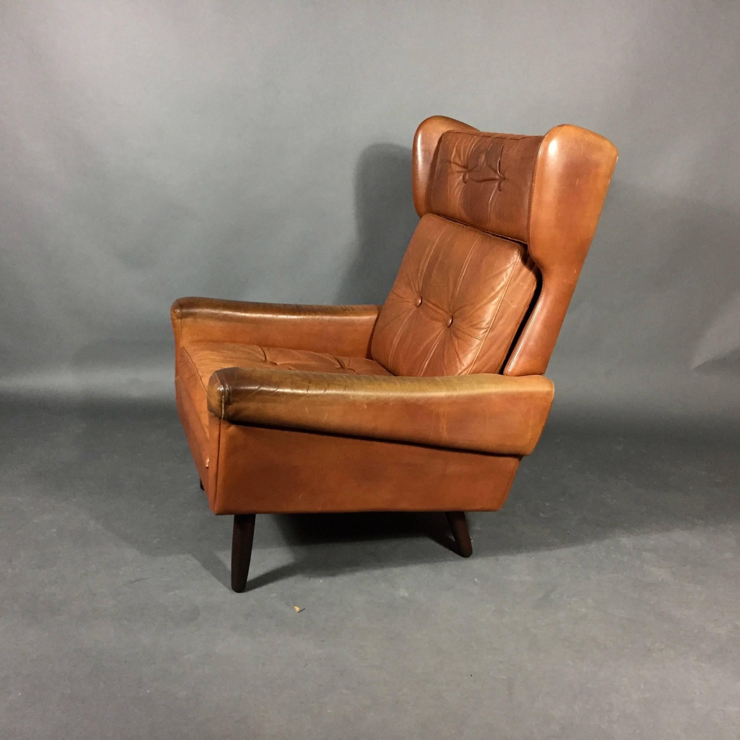 A classic vintage high-back lounge chair by Svend Skipper with diminutive wings, soft tufted leather and round-tapered stained beech legs. Three loose cushions with top snap closure. Skipper Møbler, Denmark, circa 1970. Wear to arms.