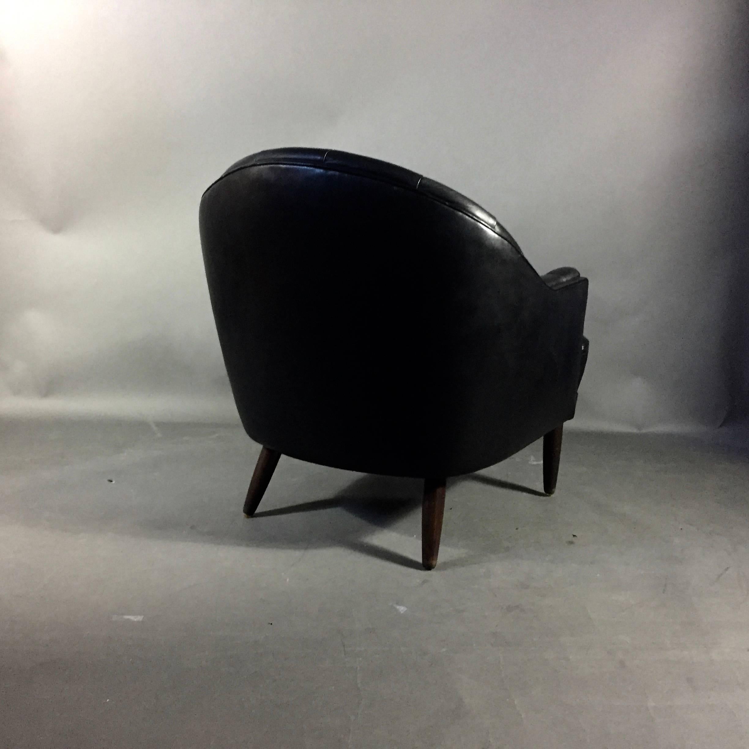 Likely Danish design from the late 1960s or early 1970s with a field of deep tufting along beautifully curved seat back and arms - all in chic black leather. Beech legs. In excellent condition.