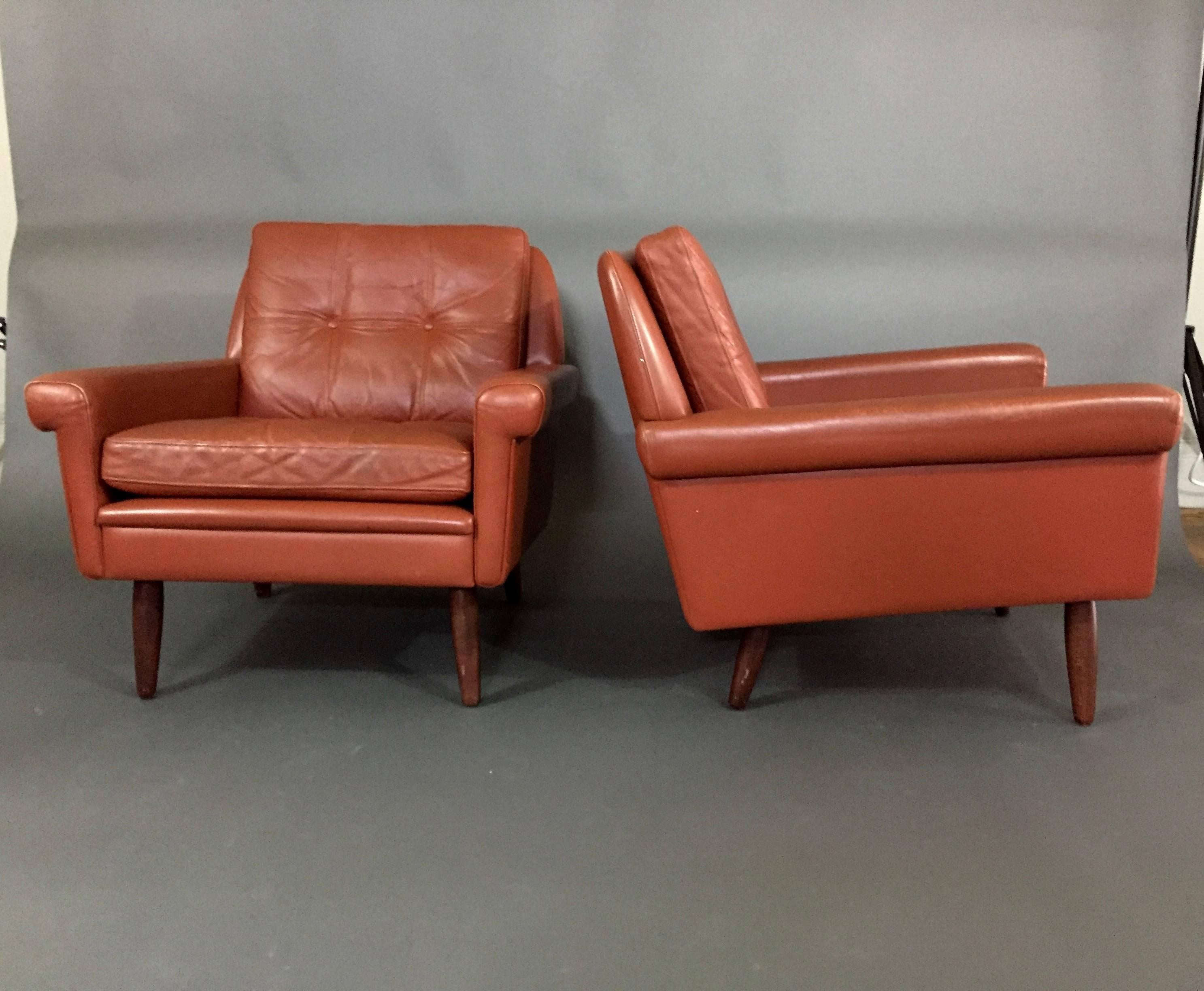 A classic pair of lounge chairs with beautifully squared arms and tampered back with two loose and buttoned cushions - all in a medium red/orange leather that speaks perfectly to era in which they were created. Danish producer - 1960s.  Similar to