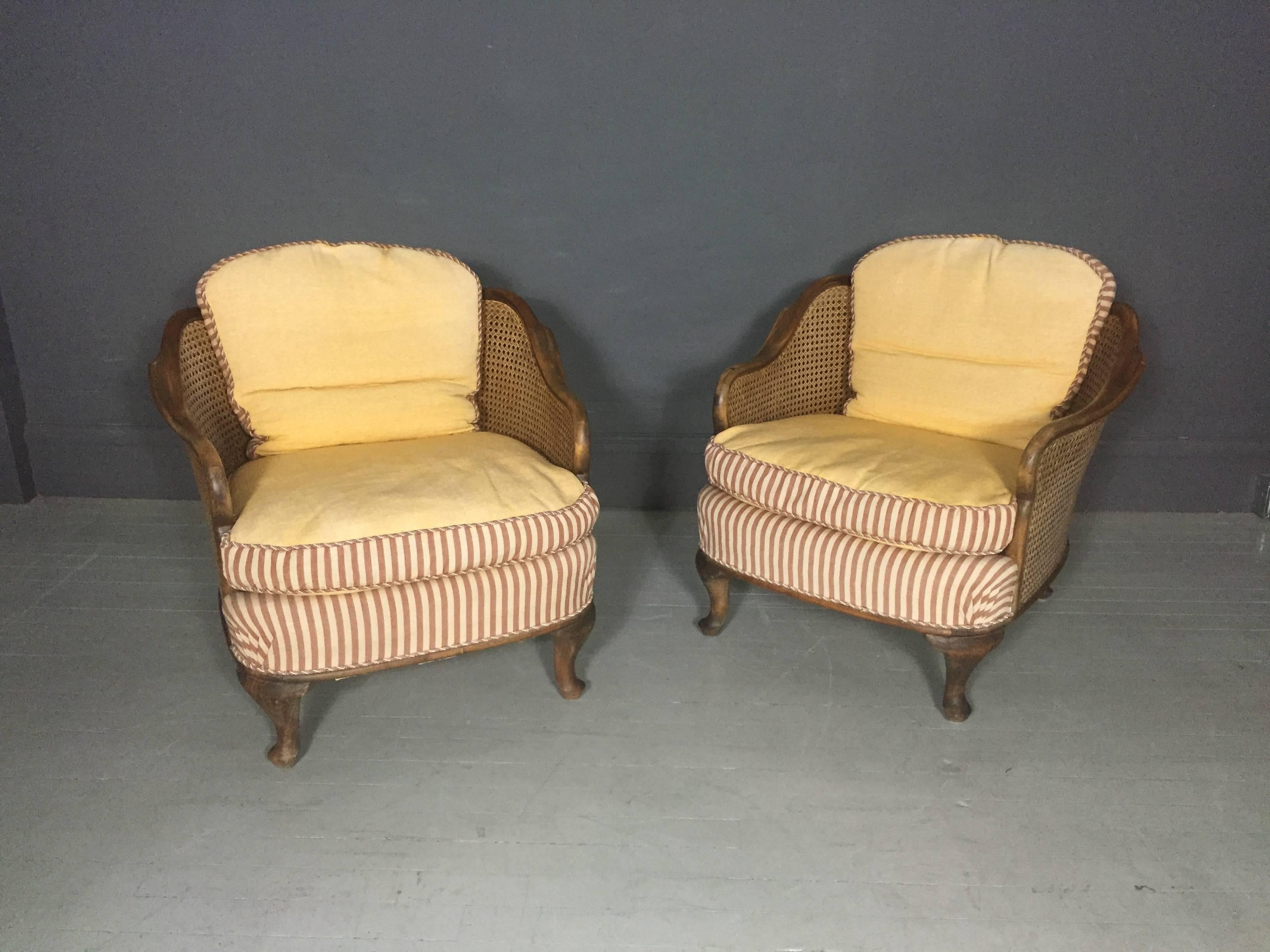 A lovely pair of tub chairs in the Bergere style with double woven cane on sides and back, sculpted walnut frames, short cabriole or pad-foot legs, wonderful yellow ribbed-brocade upholstery with deep-rose striped cotton front, matching corded trim,