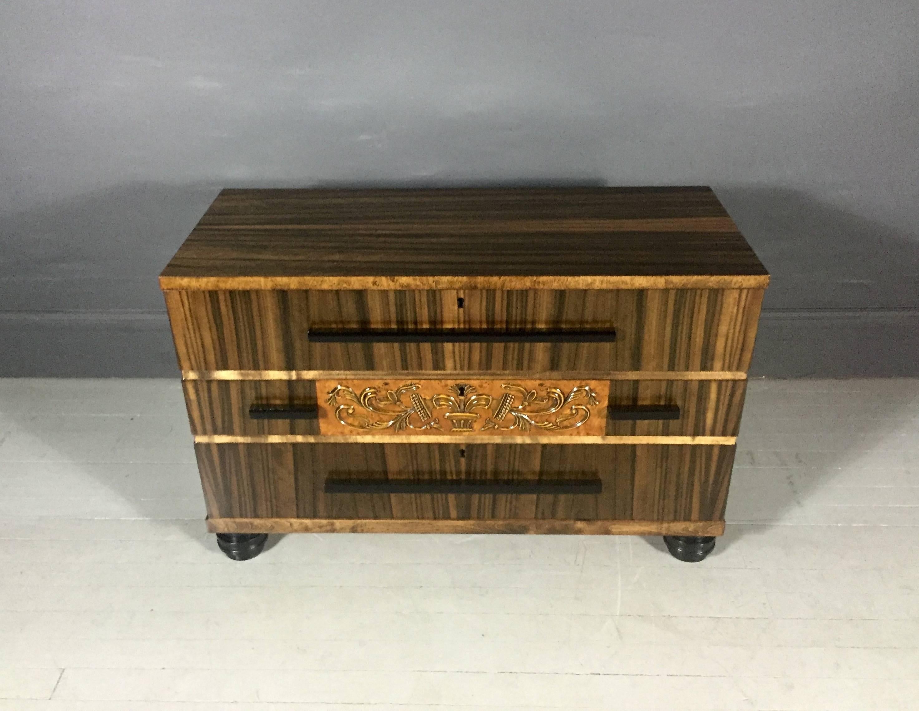 Deeply beautiful bureau in full Zebrano veneer (Zebra wood Miscoberlinia) in the style transition between Art Nouveau and Art Deco, three drawers with black painted long-pulls, center decoration in gold-gilt metal, black painted Art Deco carved