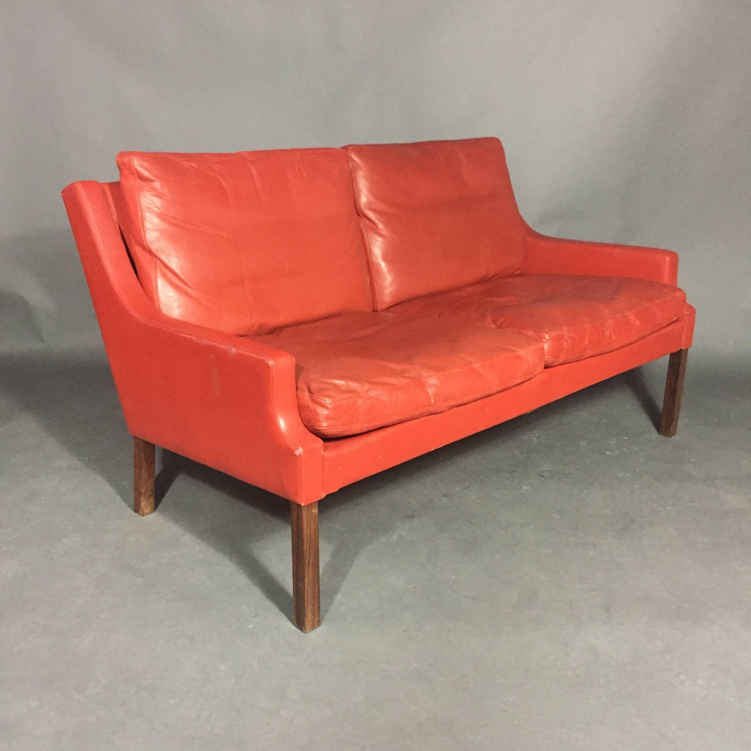 A gorgeous red/orange two-seat leather sofa by Georg Thams with rosewood legs and four loose cushions. Leather is soft and supple, Manufactured by Vejen Polstermøbelfabrik (attached labels), Denmark, 1950s-1960s. Minor scuffs and small break in arm