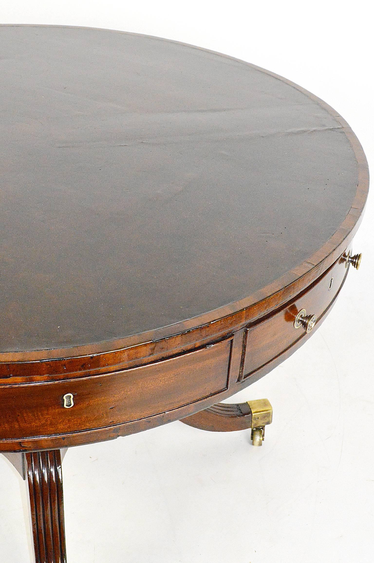 English mahogany inlaid leather top rent/drum table top sitting on four column pedestal terminating on saber legs resting on original brass casters. Late 18th or early 19th century.