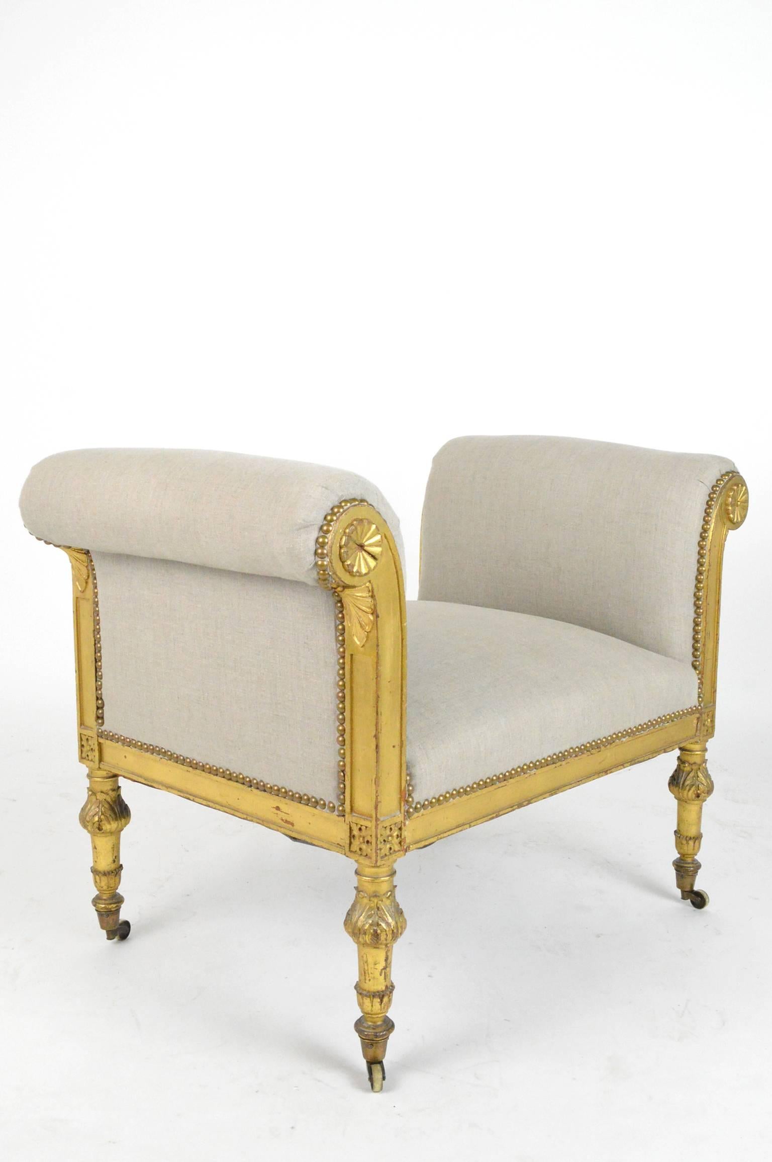 French giltwood bench or window seat, raised on four fluted column legs ending on brass casters and reupholstered in a linen fabric.