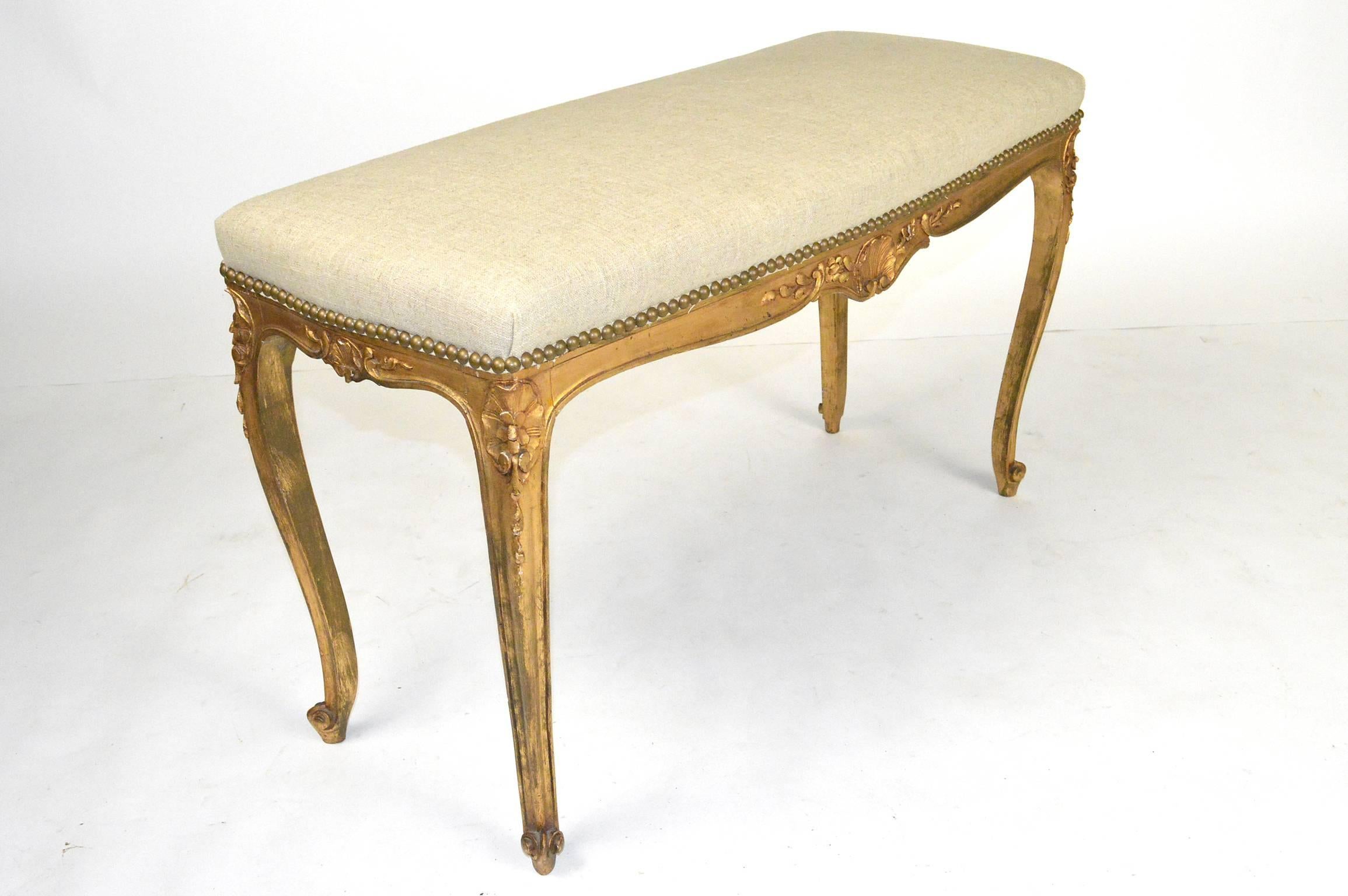 French Louis XVI style carved and giltwood bench covered in linen upholstery with nailhead trim.