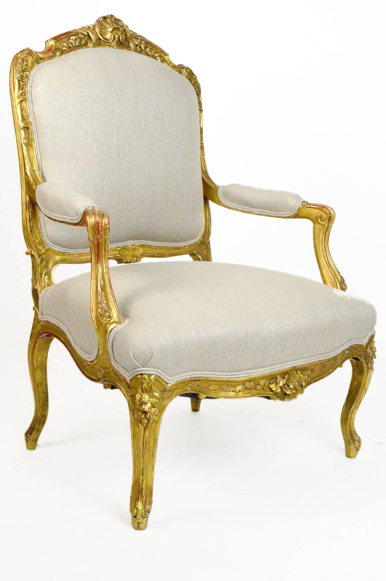 19th century Louis XV style giltwood armchair with elegant hand carving to top, apron, arms and legs. Upholstered in neurtral linen.